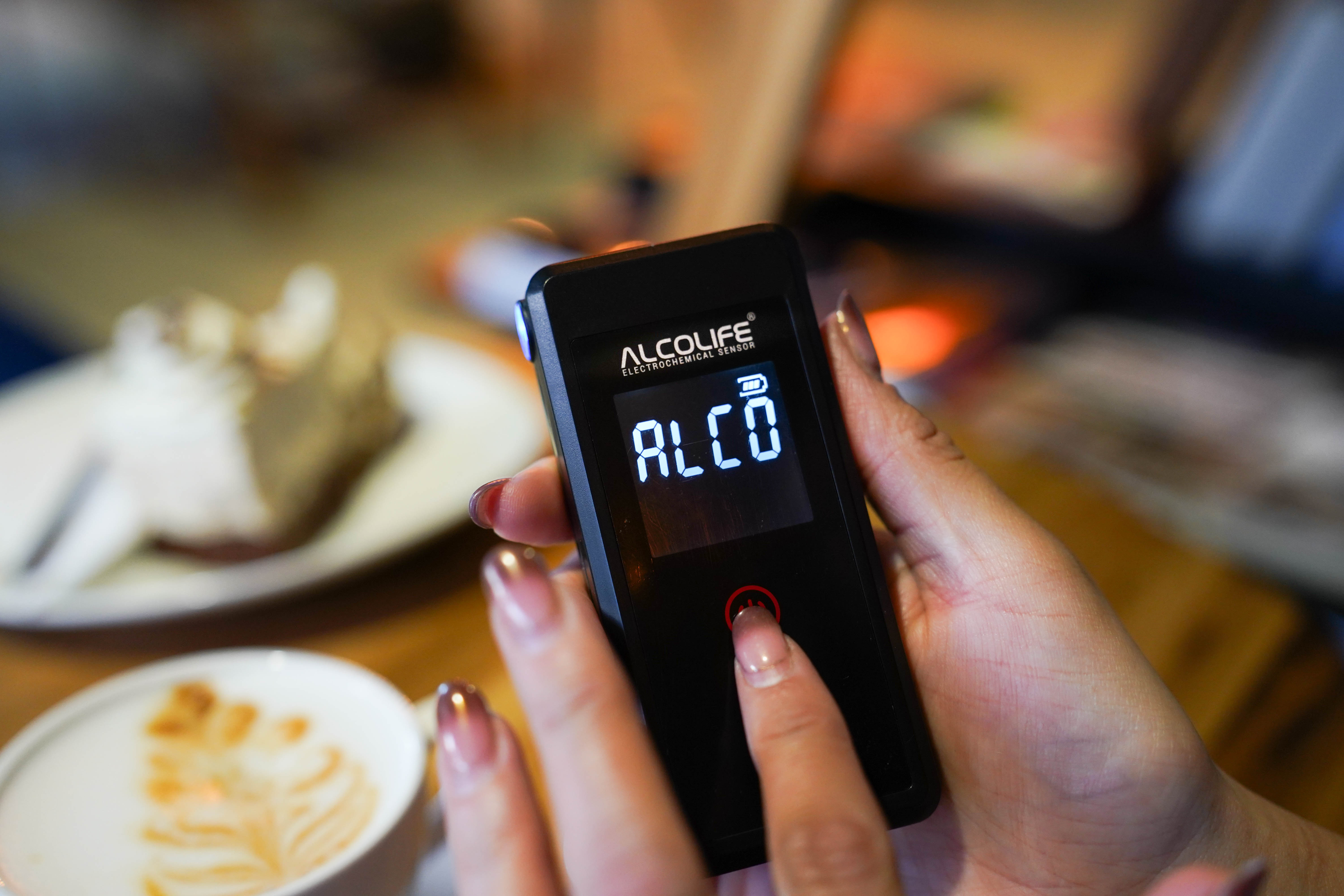 Dłoń trzymająca czarny alkomat z podświetlanym wyświetlaczem.