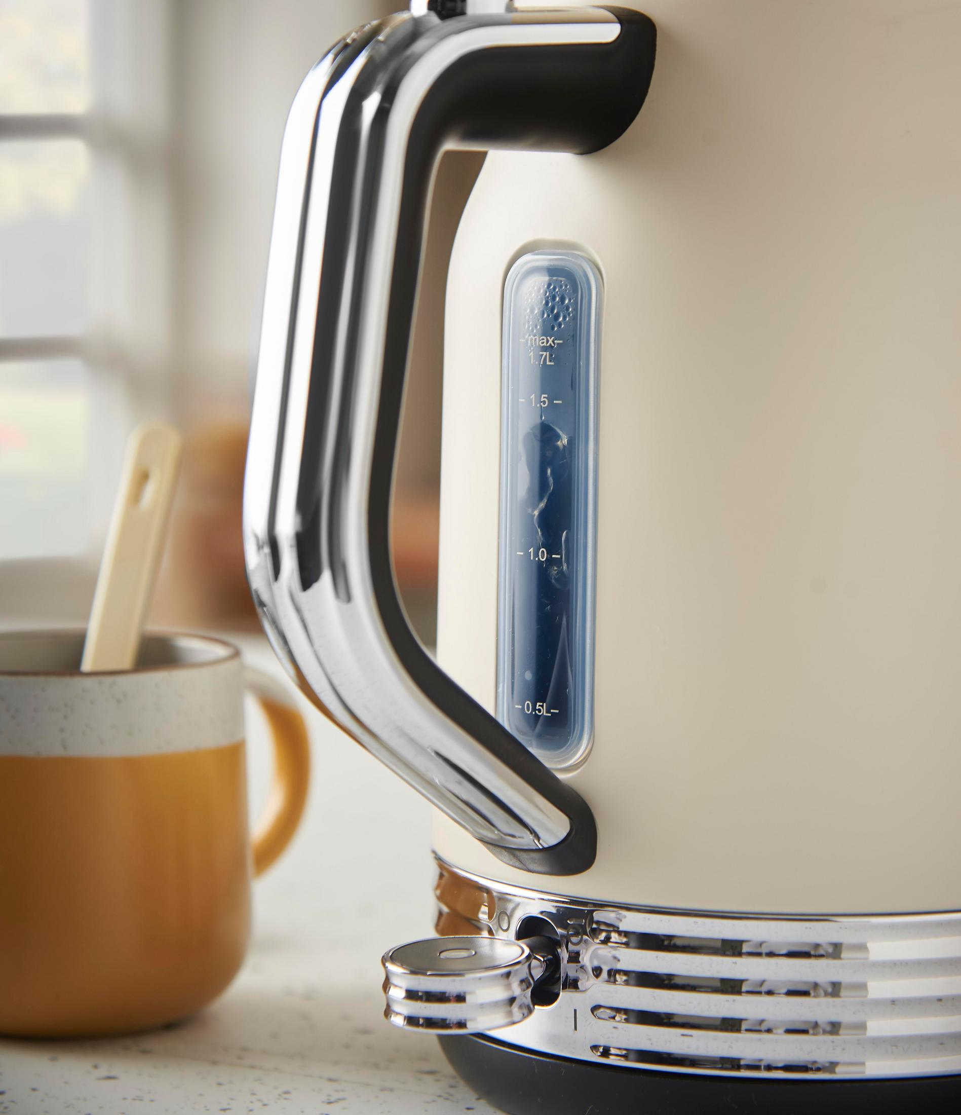 Ein cremefarbener Wasserkocher mit Chromdetails, neben einer gelben Tasse.