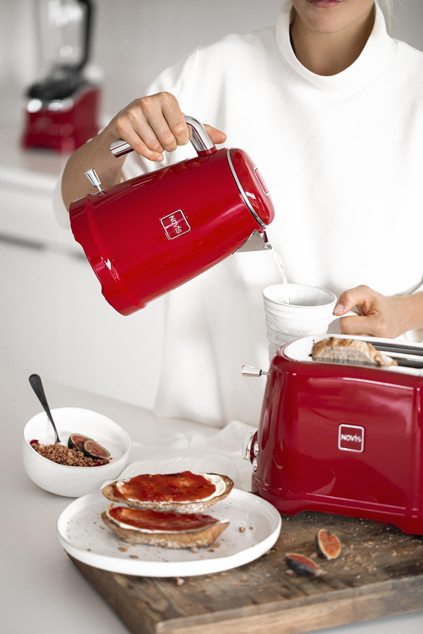 Un bollitore rosso Novis versa acqua in una tazza. Colazione sul tavolo.