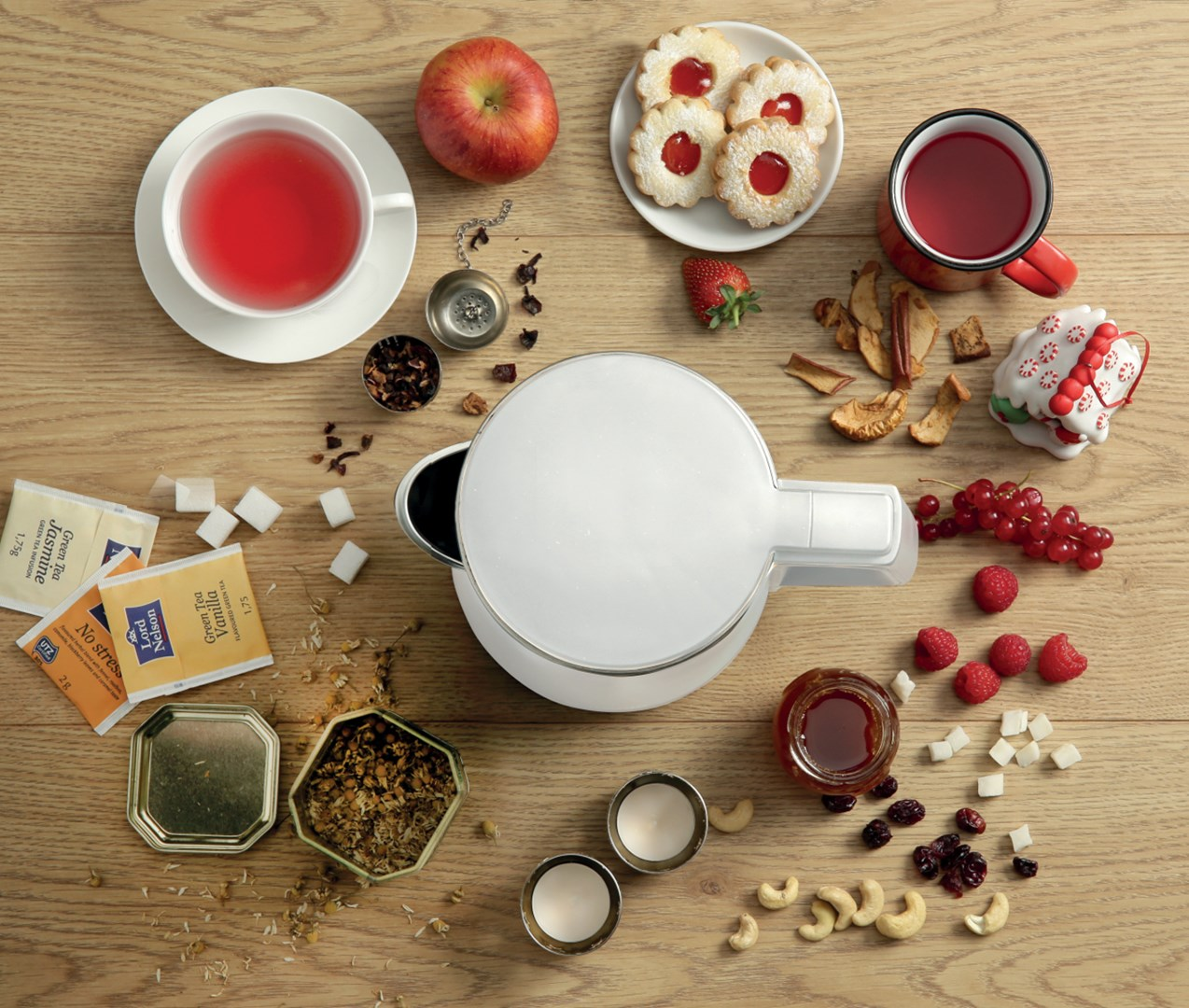 Czajnik, filiżanki, ciasteczka, owoce i słodycze ułożone na drewnianym stole.