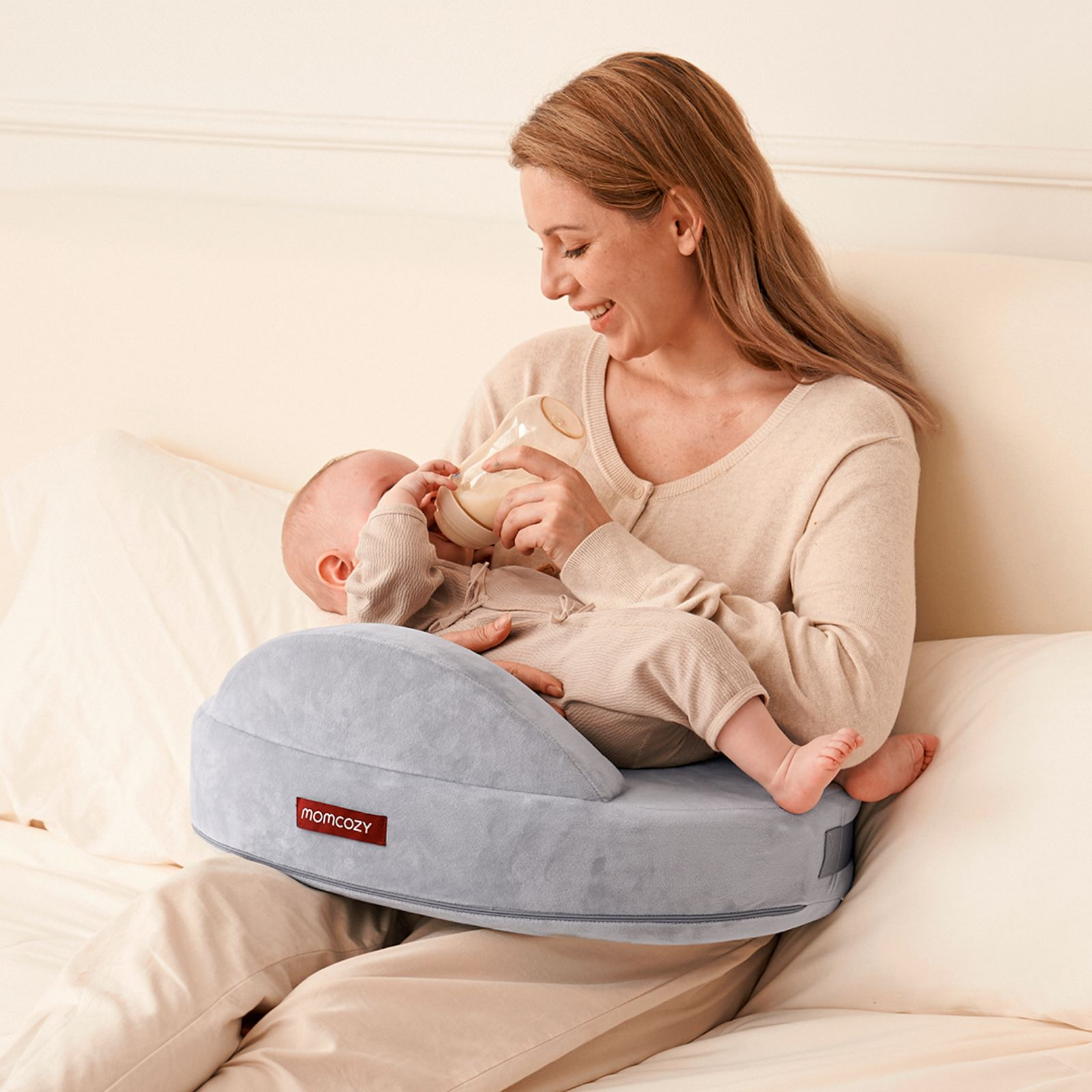 Une femme nourrit un bébé au biberon sur un coussin de soutien gris.