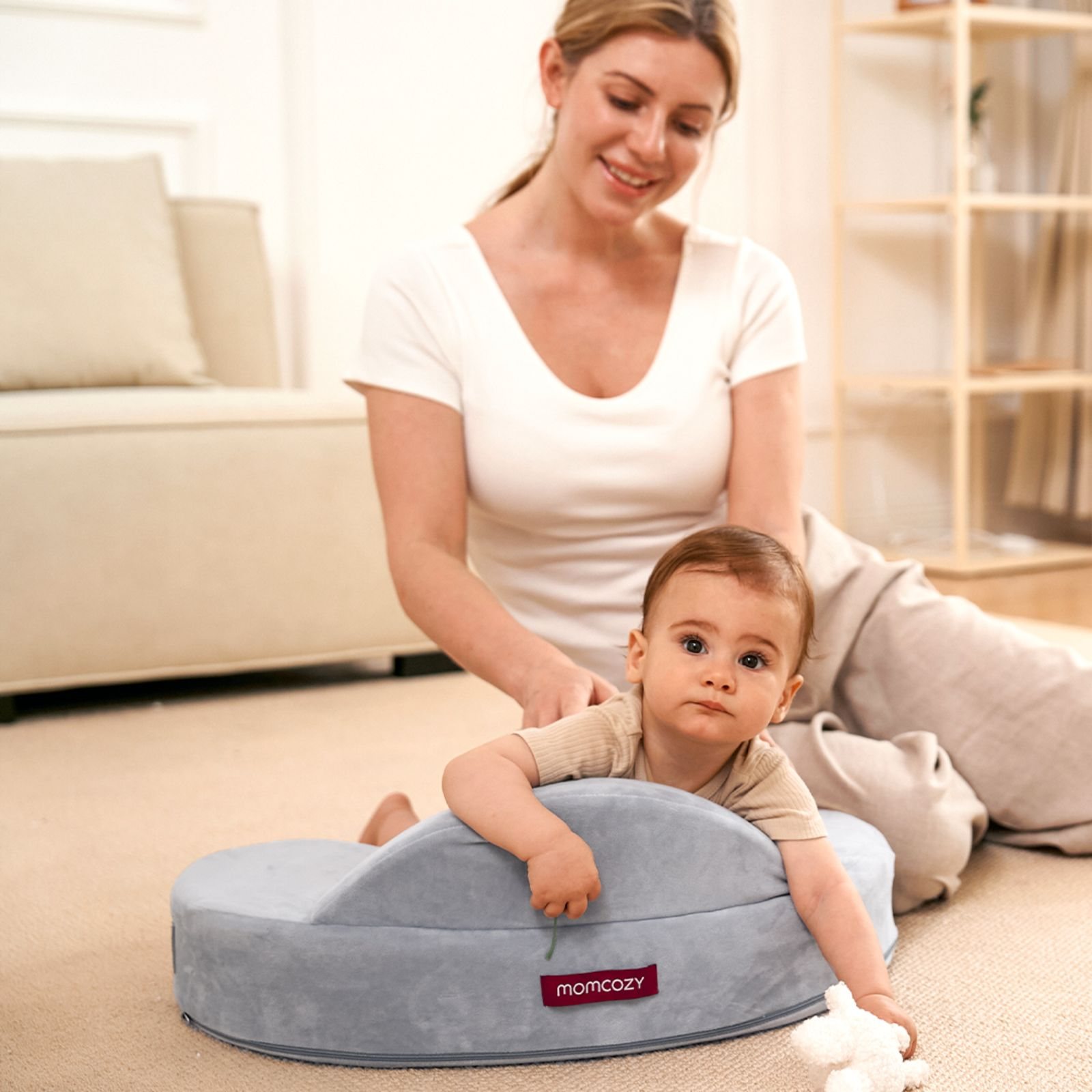 Une femme masse un bébé allongé sur un coussin gris. Un jouet est à côté.