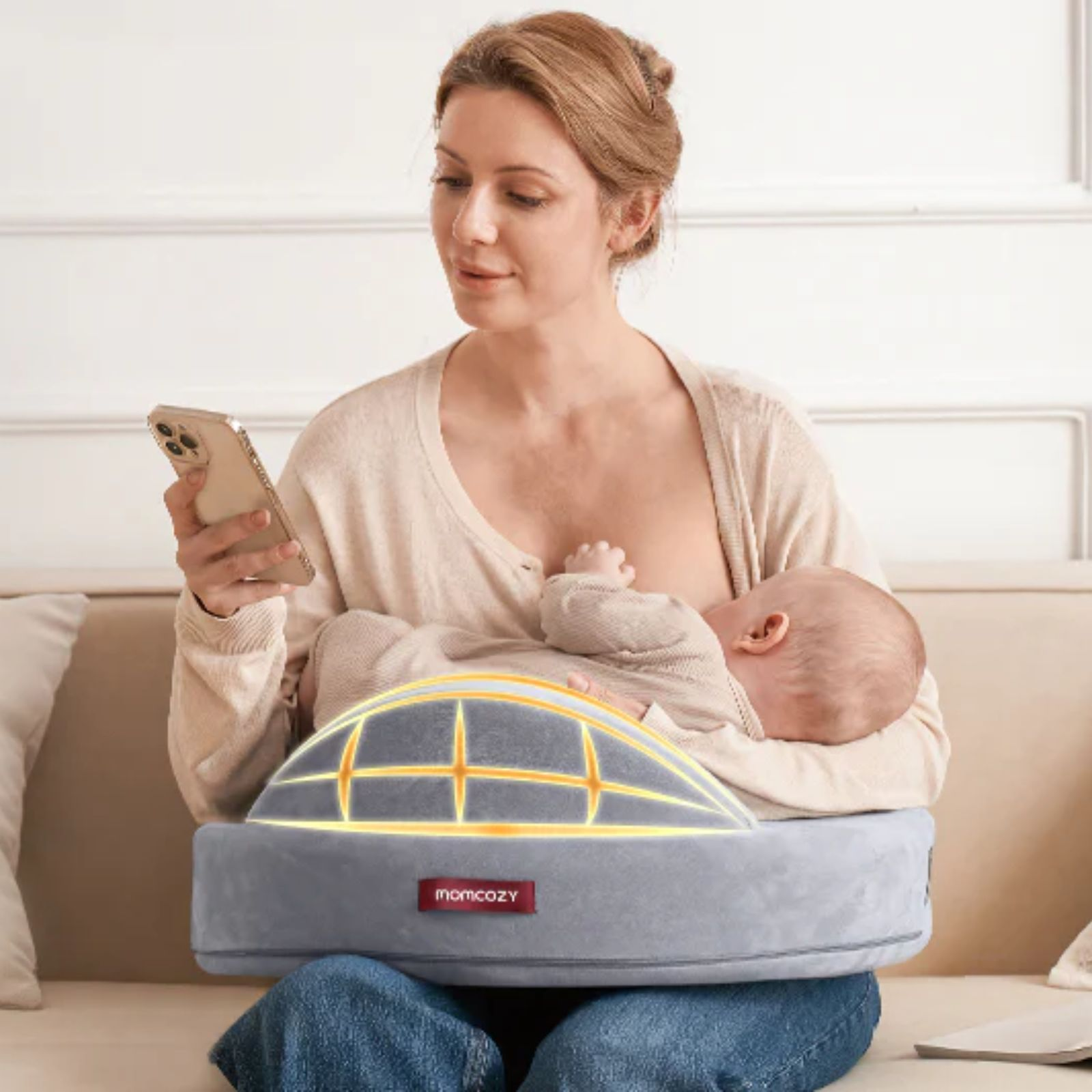 Une femme assise sur un canapé tient un téléphone en allaitant un bébé.