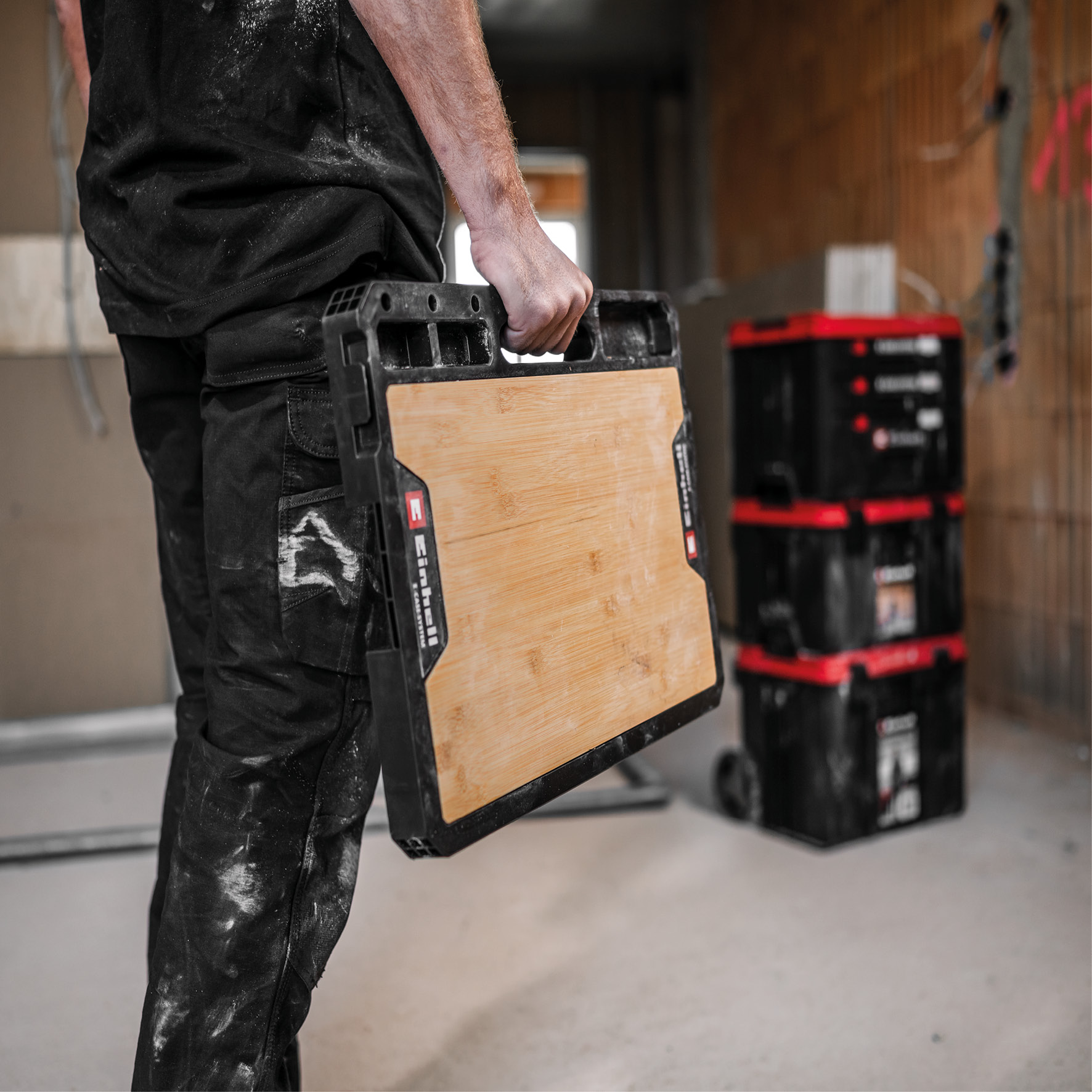Mann in schwarzer Arbeitskleidung trägt eine Holzarbeitsplatte mit schwarzem Rahmen.