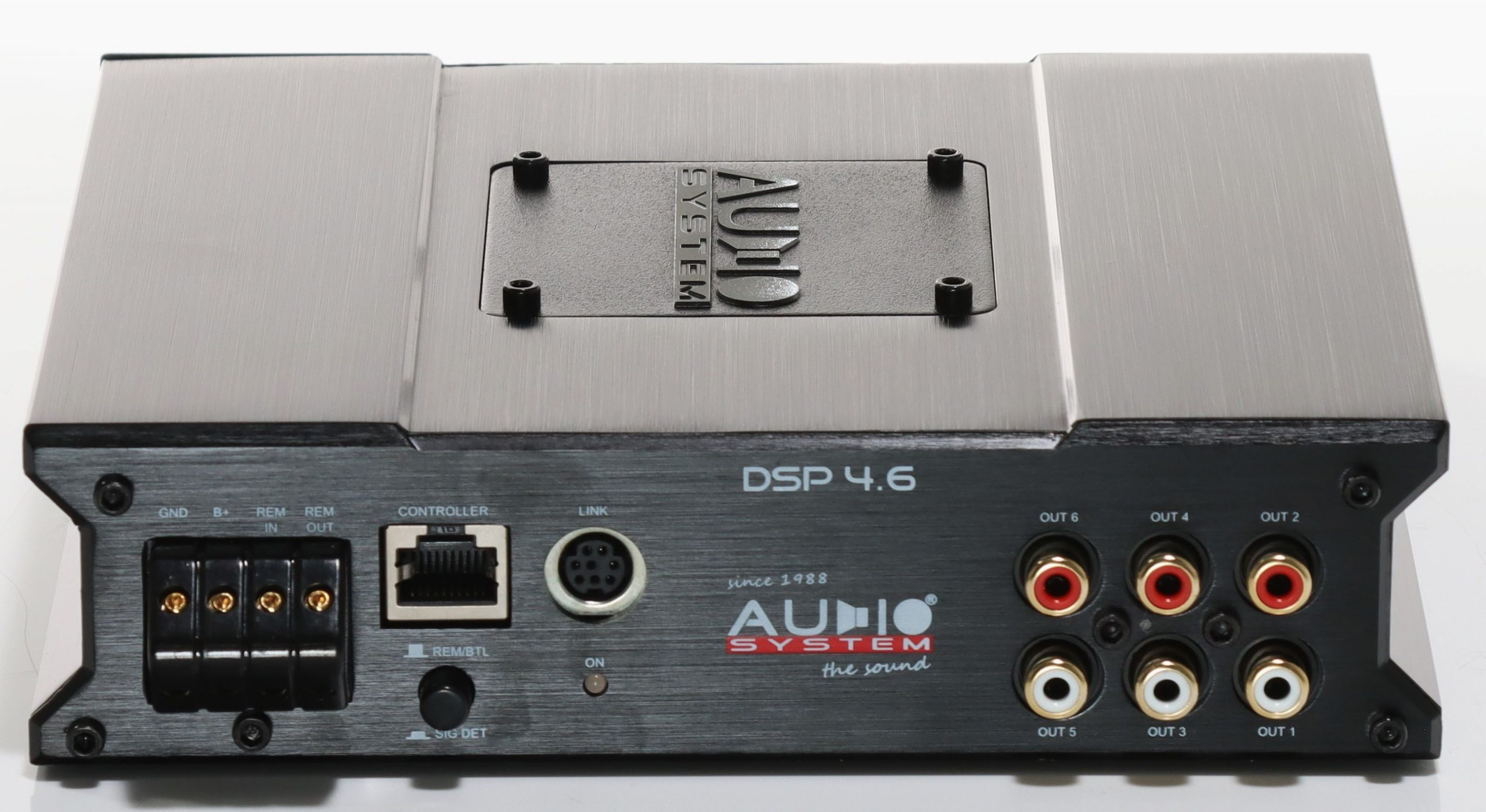 Ein silberner Audioverstärker mit beschrifteten Anschlüssen und dem Logo 'AUDIO SYSTEM'.