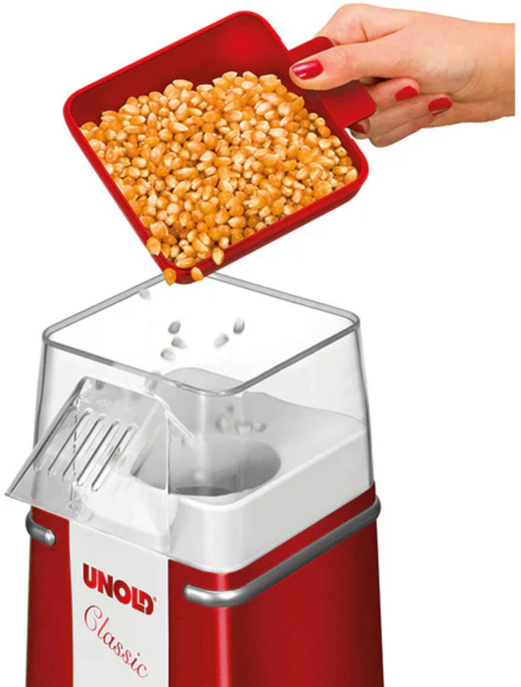 Una cuchara roja llena de granos de maíz se vierte en una máquina de palomitas roja.