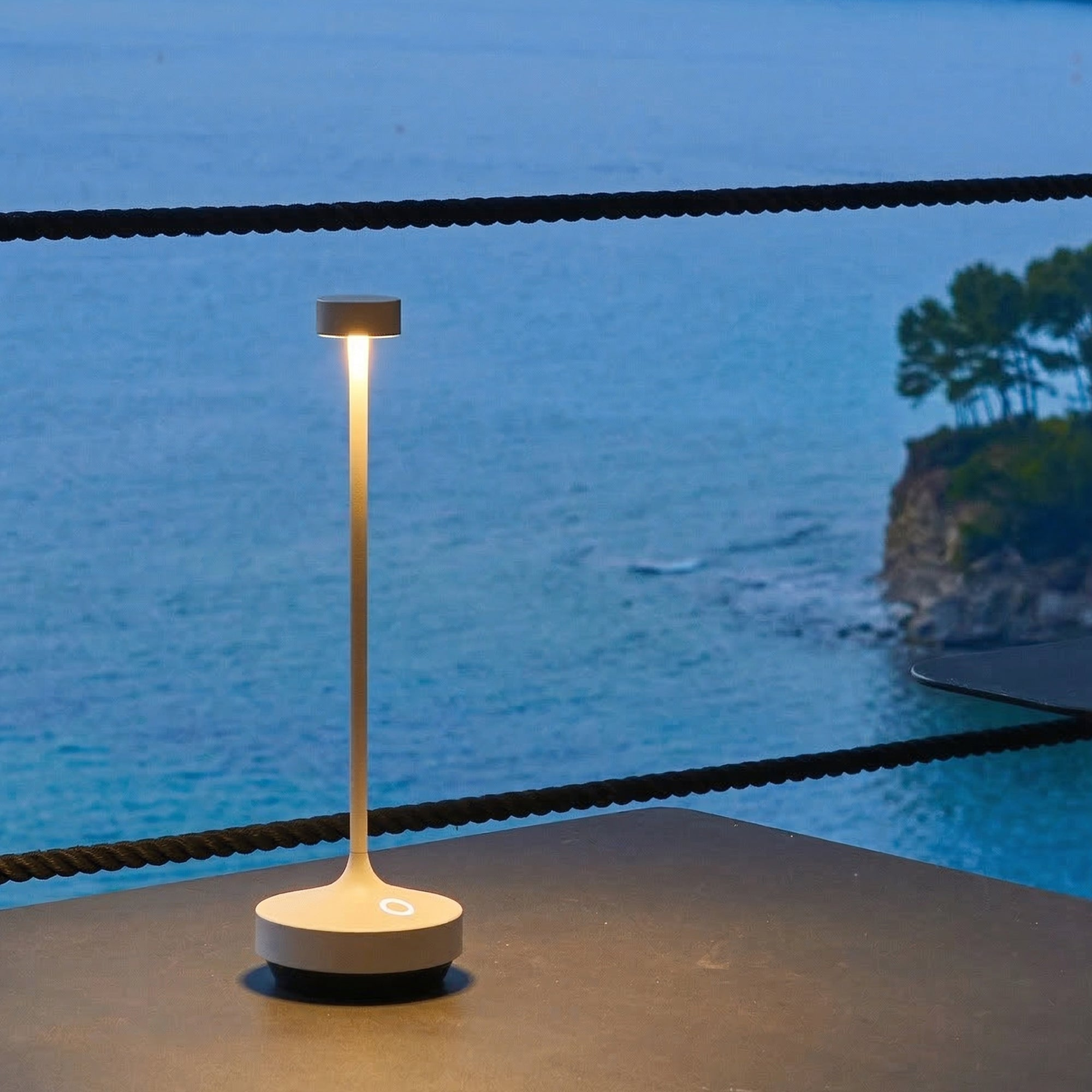Eine weiße Tischlampe leuchtet auf einem Tisch am Meer.