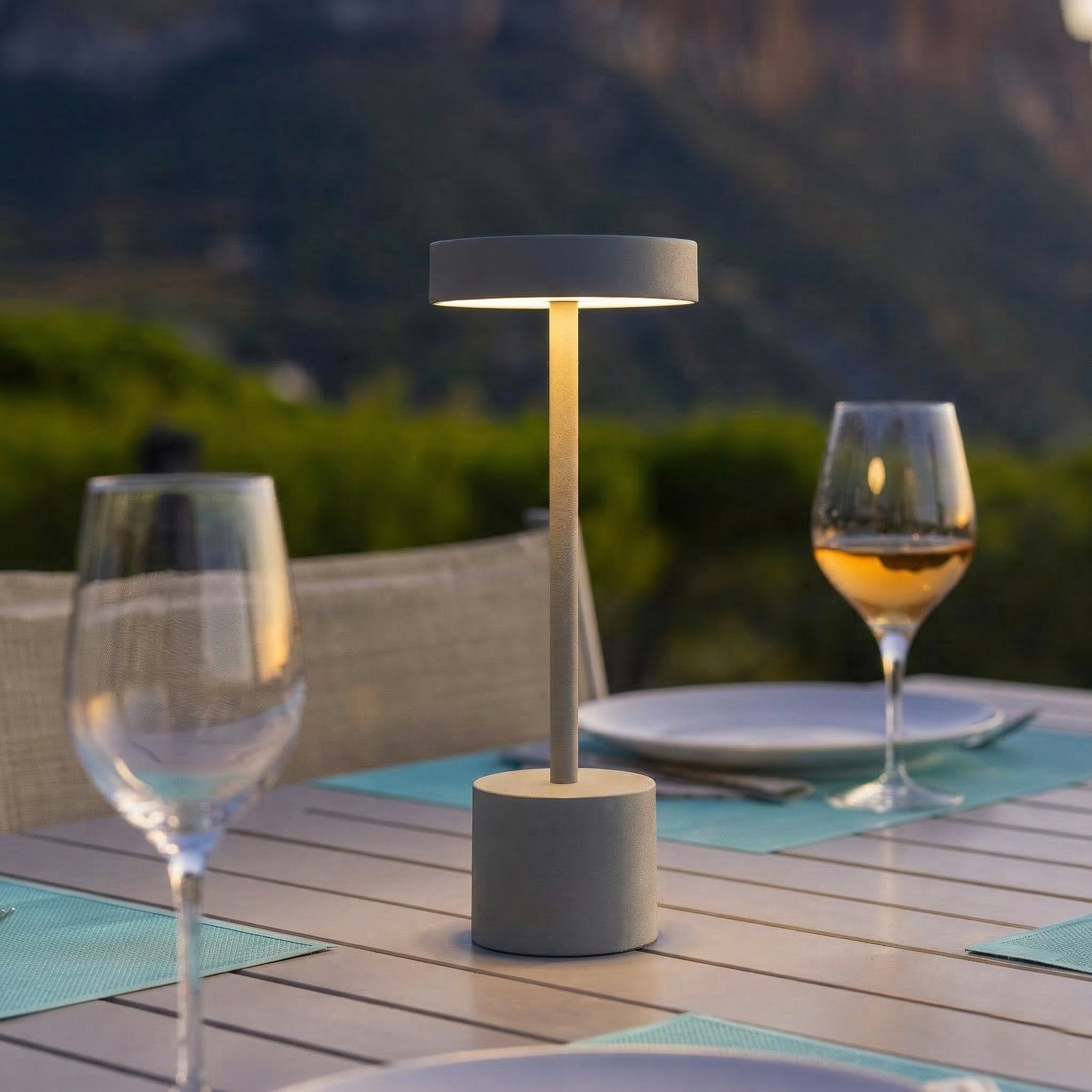 Ein Tisch mit Gläsern, Tellern und einer Lampe im Freien bei Dämmerung.