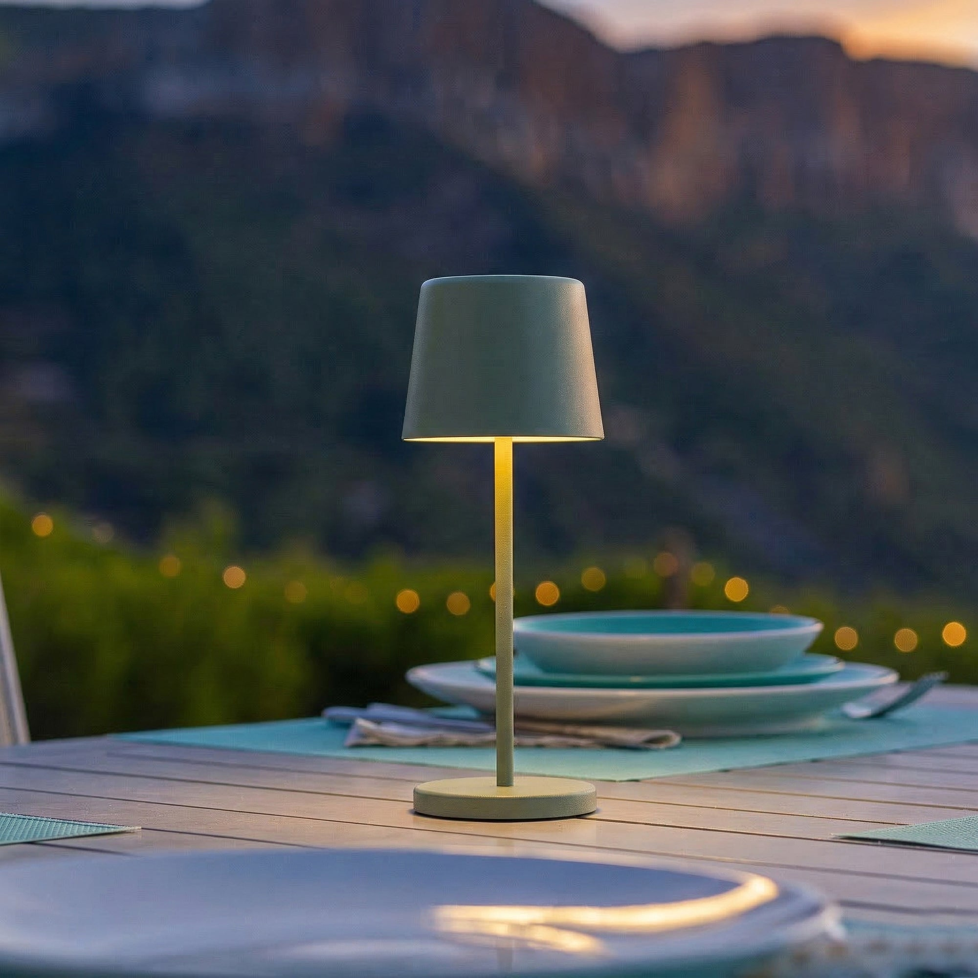 Eine graue Tischlampe leuchtet auf einem Holztisch mit Blick auf Berge.