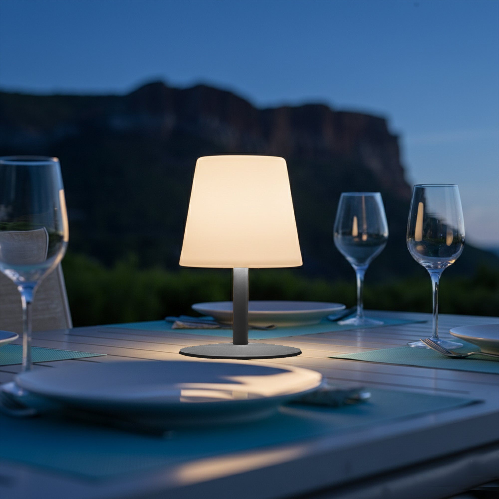Ein Tisch mit gedeckten Tellern und Gläsern bei Nacht, beleuchtet von einer Lampe.