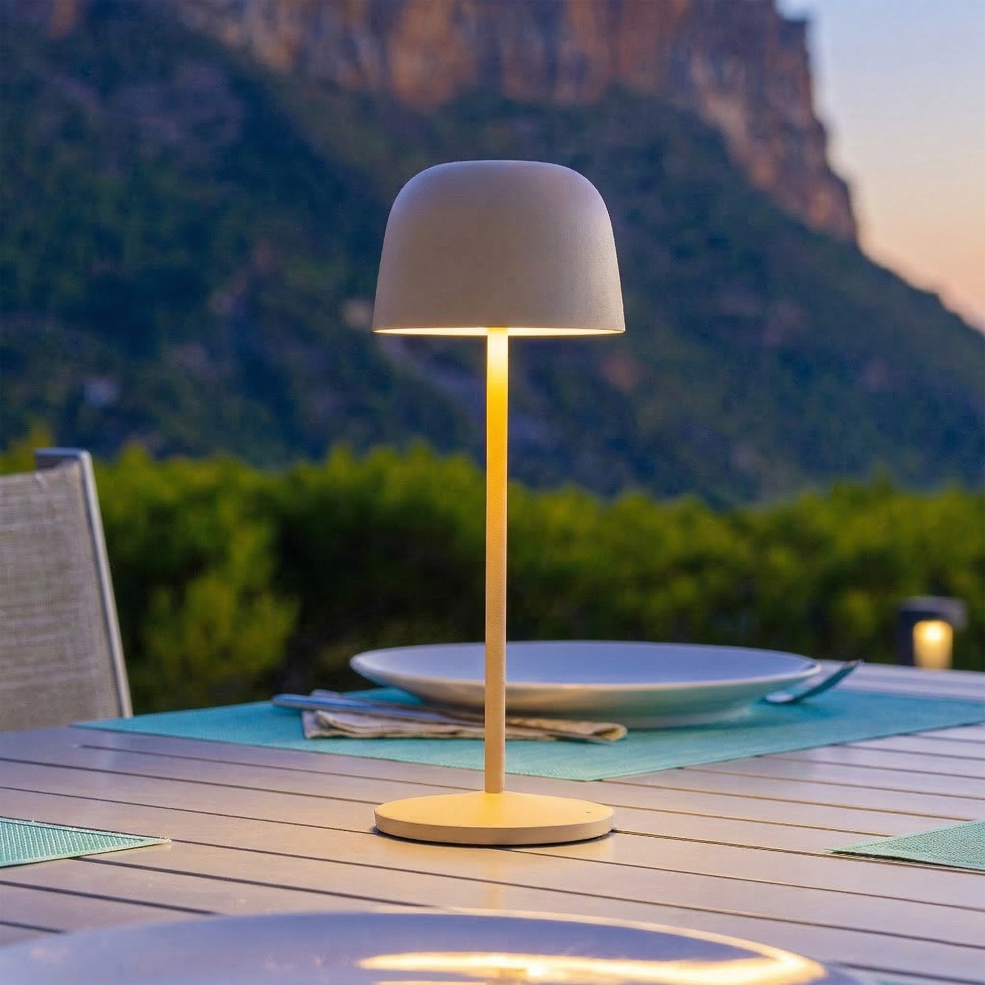 Eine Tischlampe leuchtet auf einem Tisch mit Blick auf Berge bei Dämmerung.