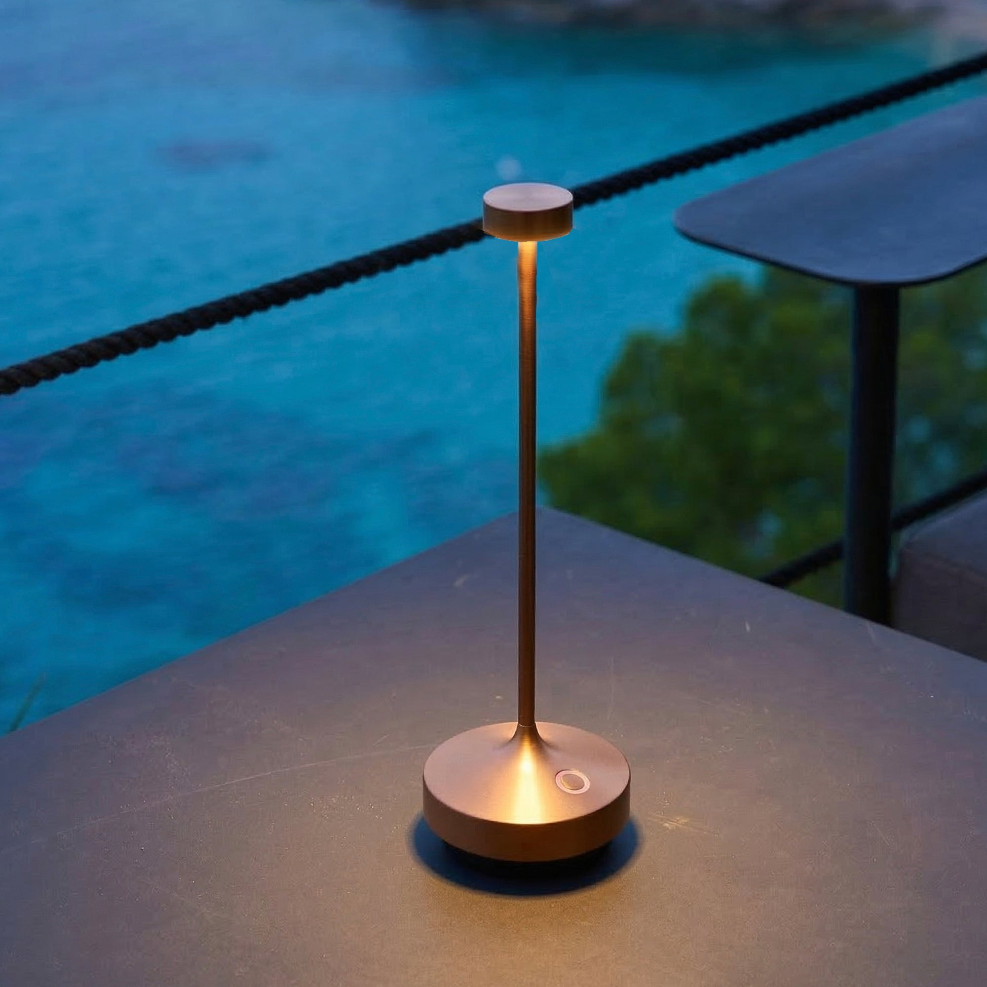 Eine kupferfarbene Tischlampe leuchtet auf einem Tisch am Wasser.