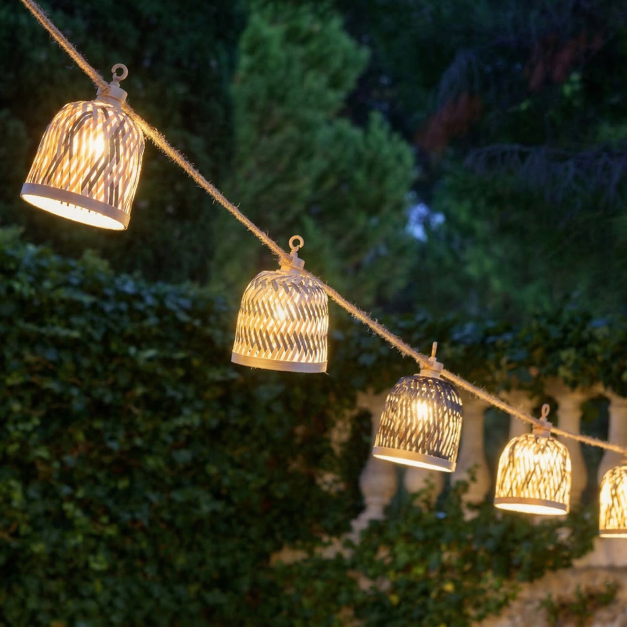 Lichterkette mit geflochtenen Lampenschirmen im Freien bei Dämmerung.
