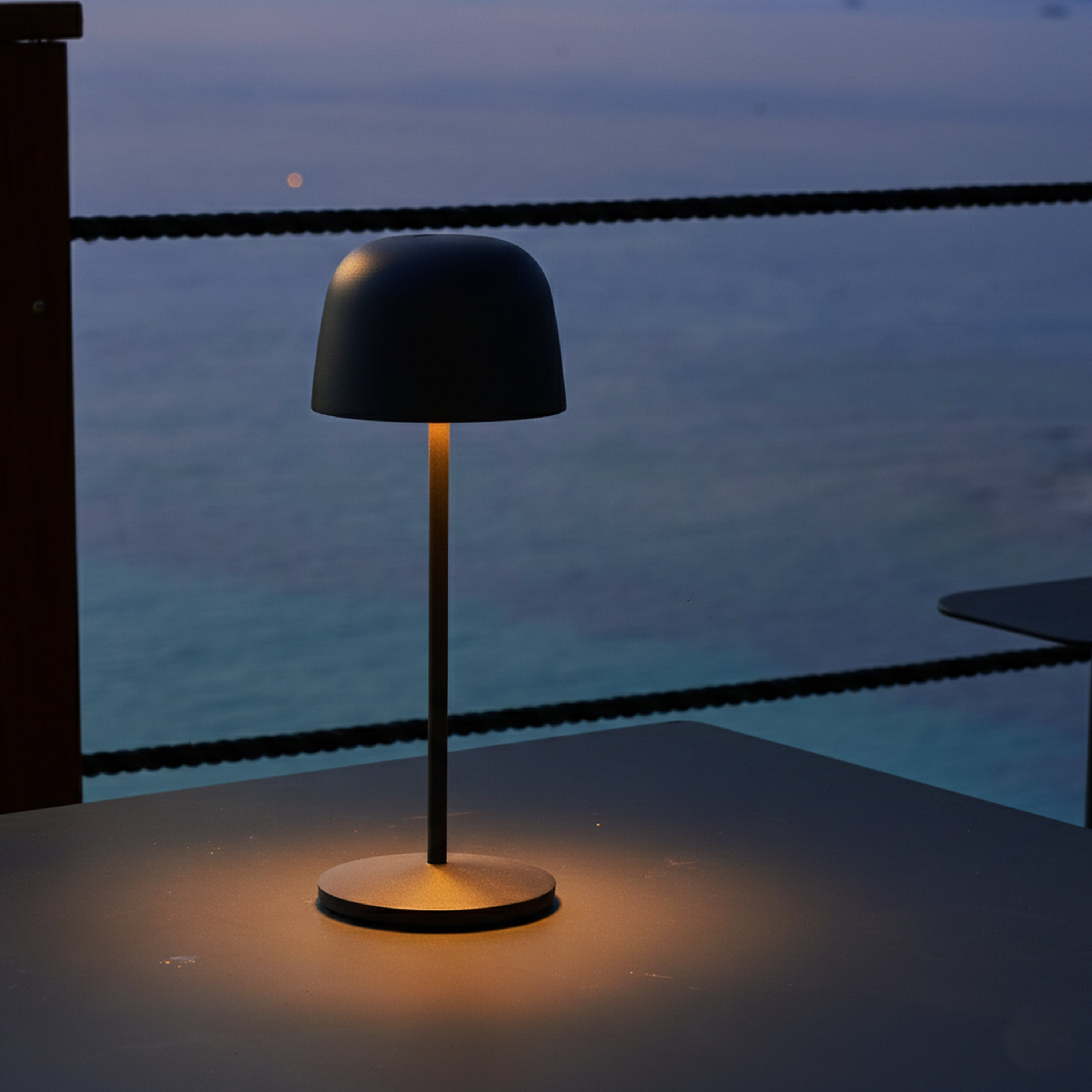 Dunkle Tischlampe leuchtet auf einem Tisch am Meer bei Dämmerung.