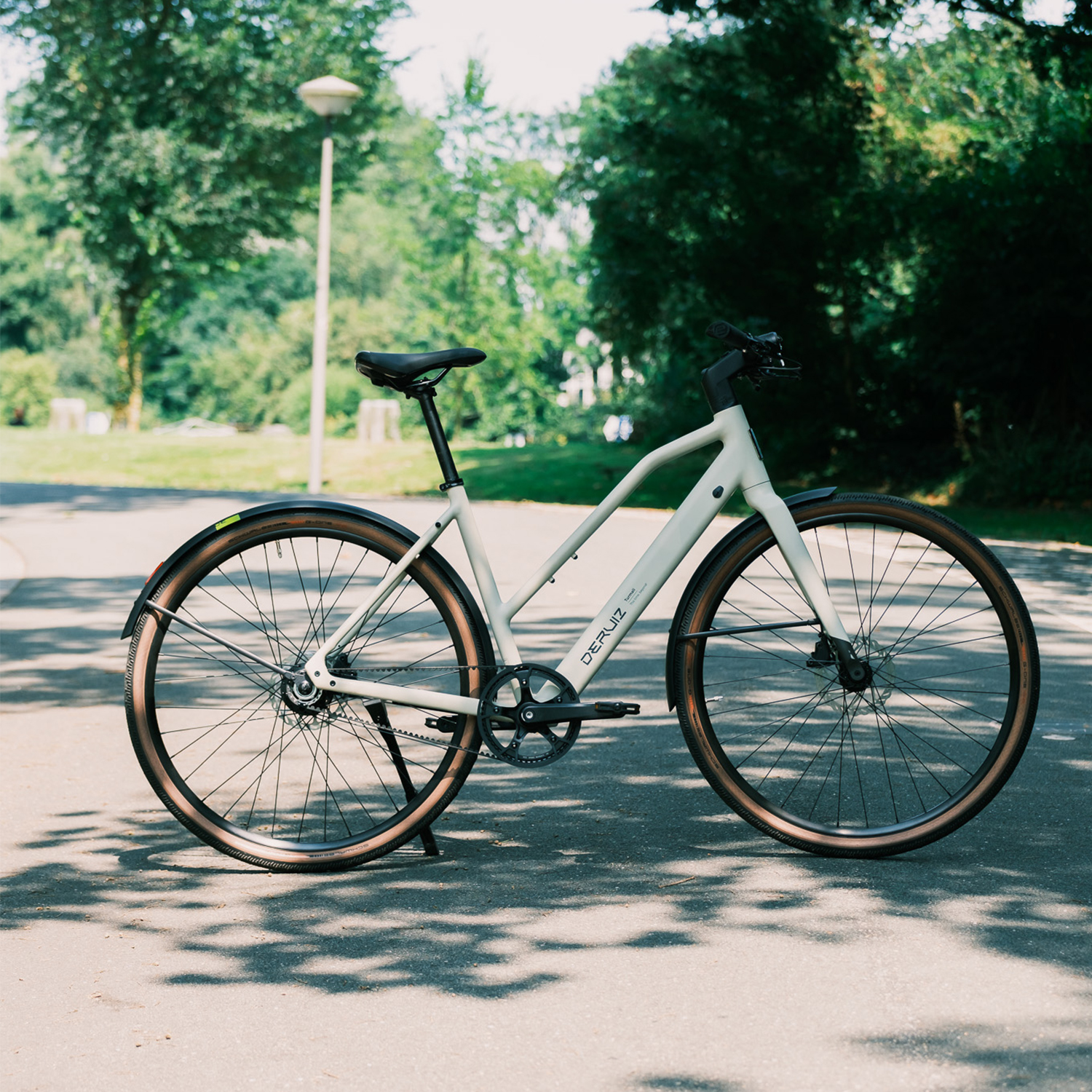 Ein hellgraues Fahrrad mit braunen Reifen steht auf einem asphaltierten Weg.