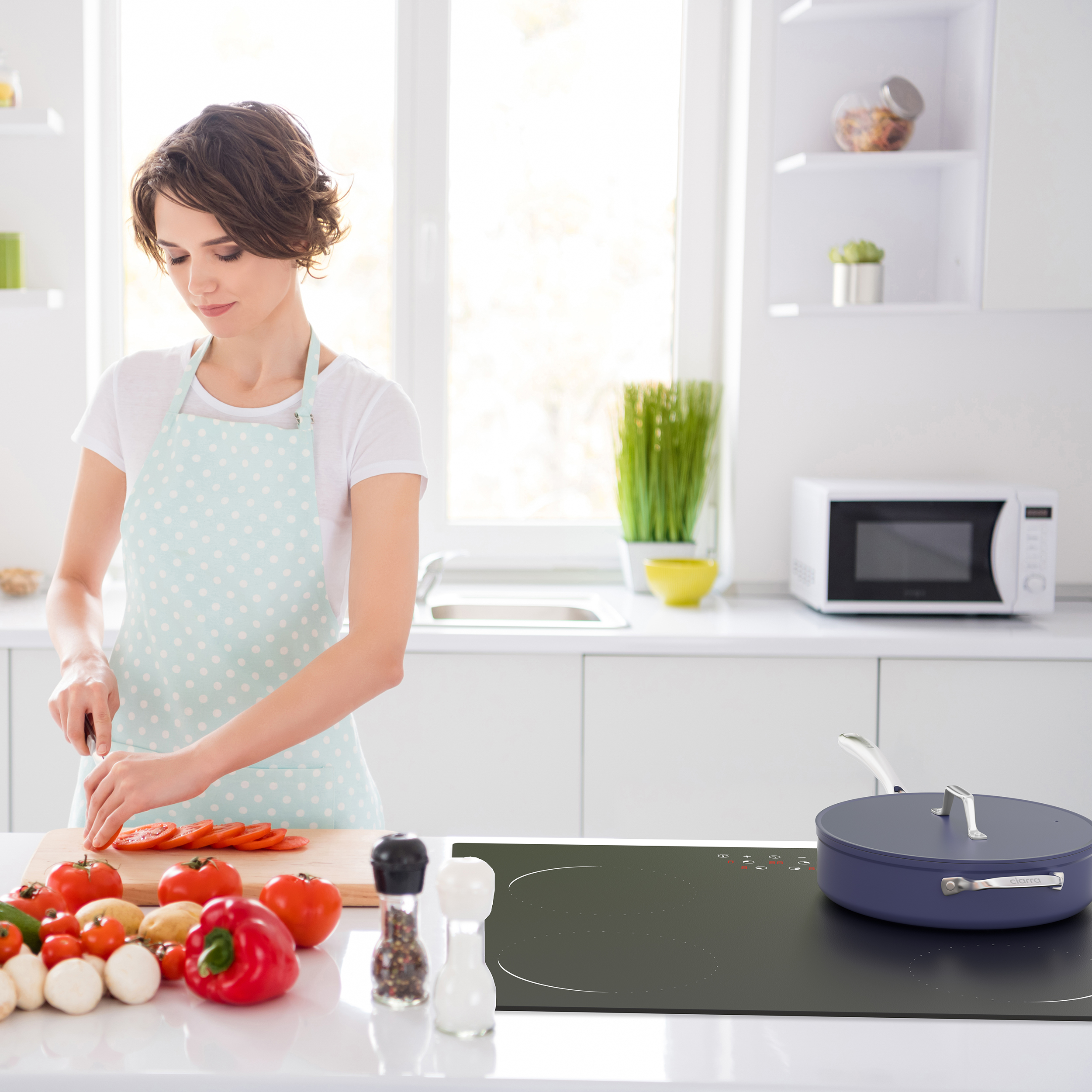 Frau schneidet Tomaten in einer modernen Küche mit frischem Gemüse auf der Arbeitsplatte.