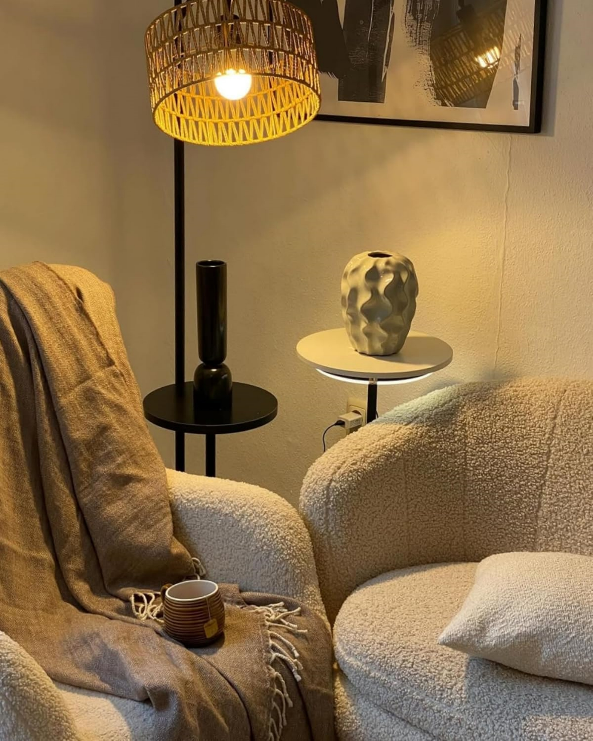 Zwei Sessel mit Kissen, Decke und Tasse Tee neben einem Stehlampen- und Vasenarrangement.