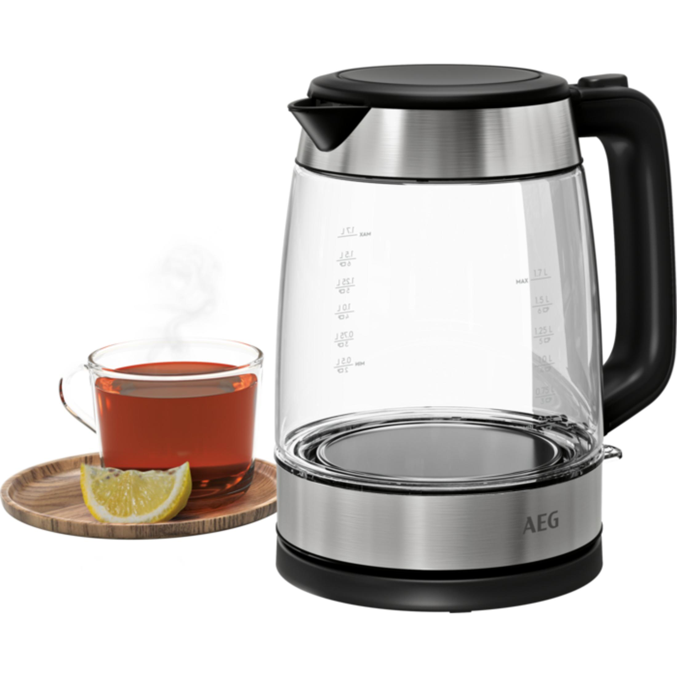 Ein Glas Wasserkocher mit schwarzem Griff und Deckel steht neben einer Tasse Tee.