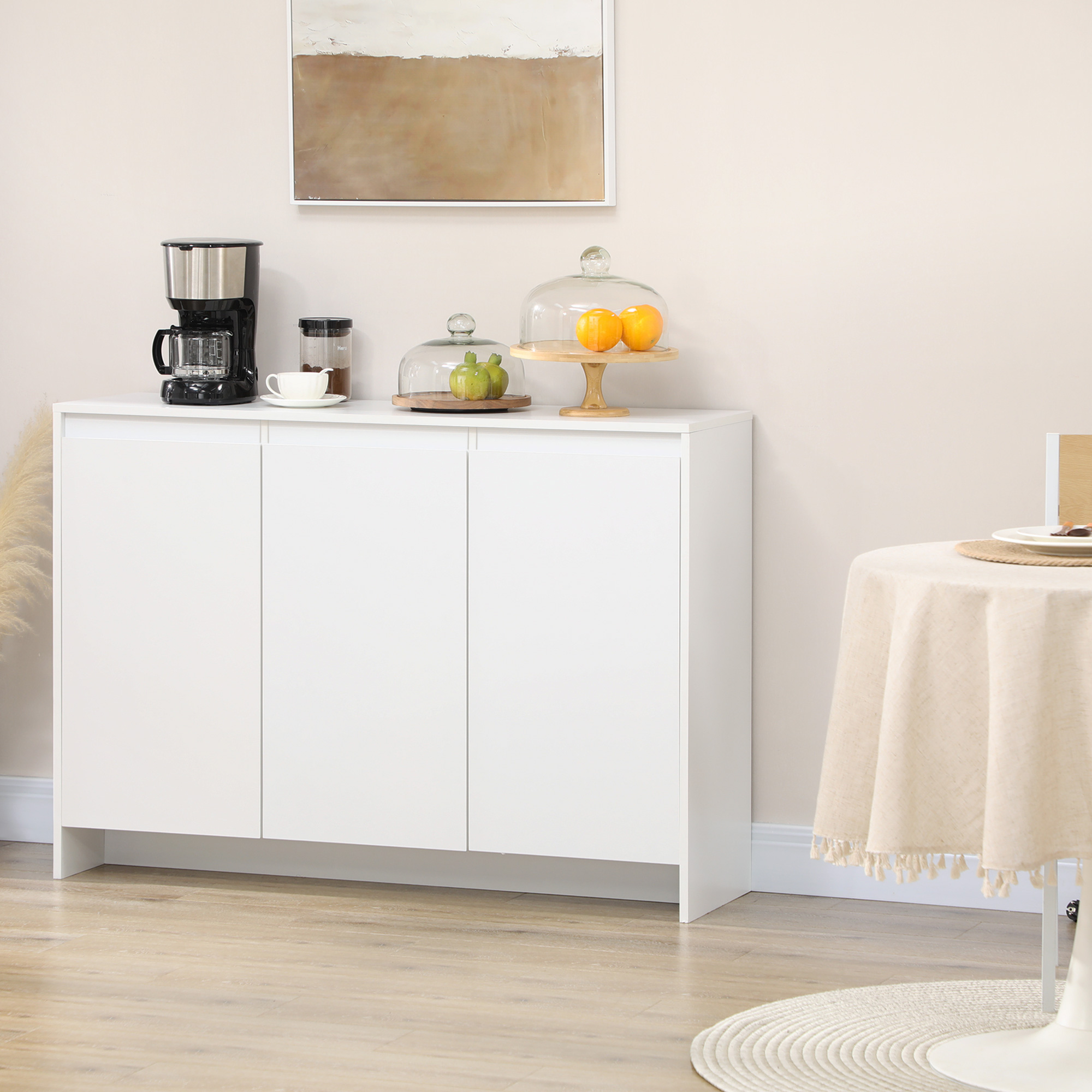Un mueble blanco con cafetera, taza y fruta bajo cúpulas de cristal.