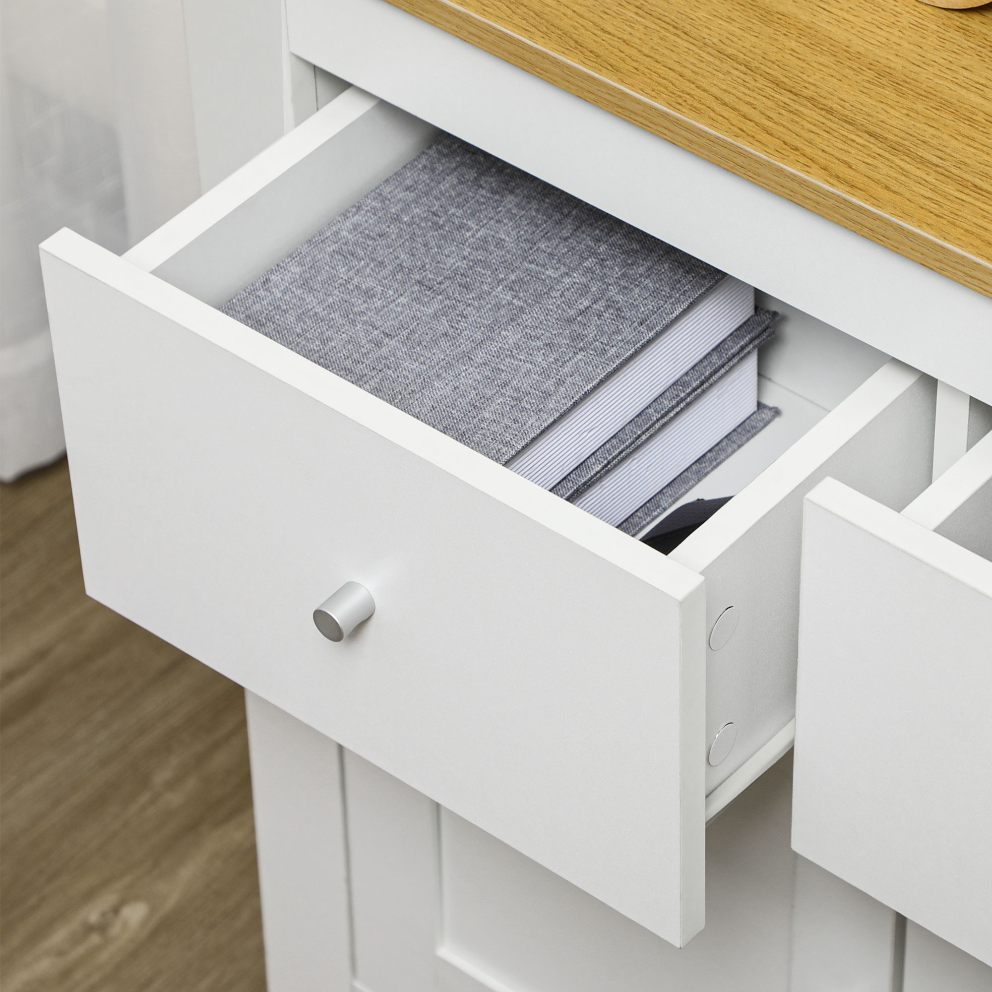 Gabinete blanco con cajón abierto. Libros grises y tela a rayas dentro.