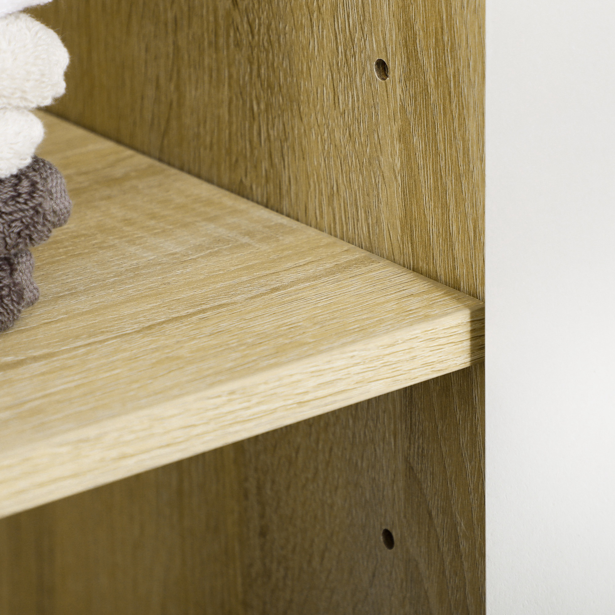 Toallas dobladas apiladas en un estante de madera clara con pared blanca.