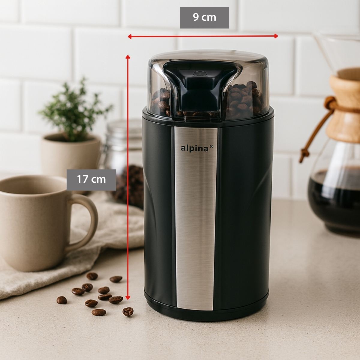 Black coffee grinder, 9x17cm, filled with beans, next to a mug.