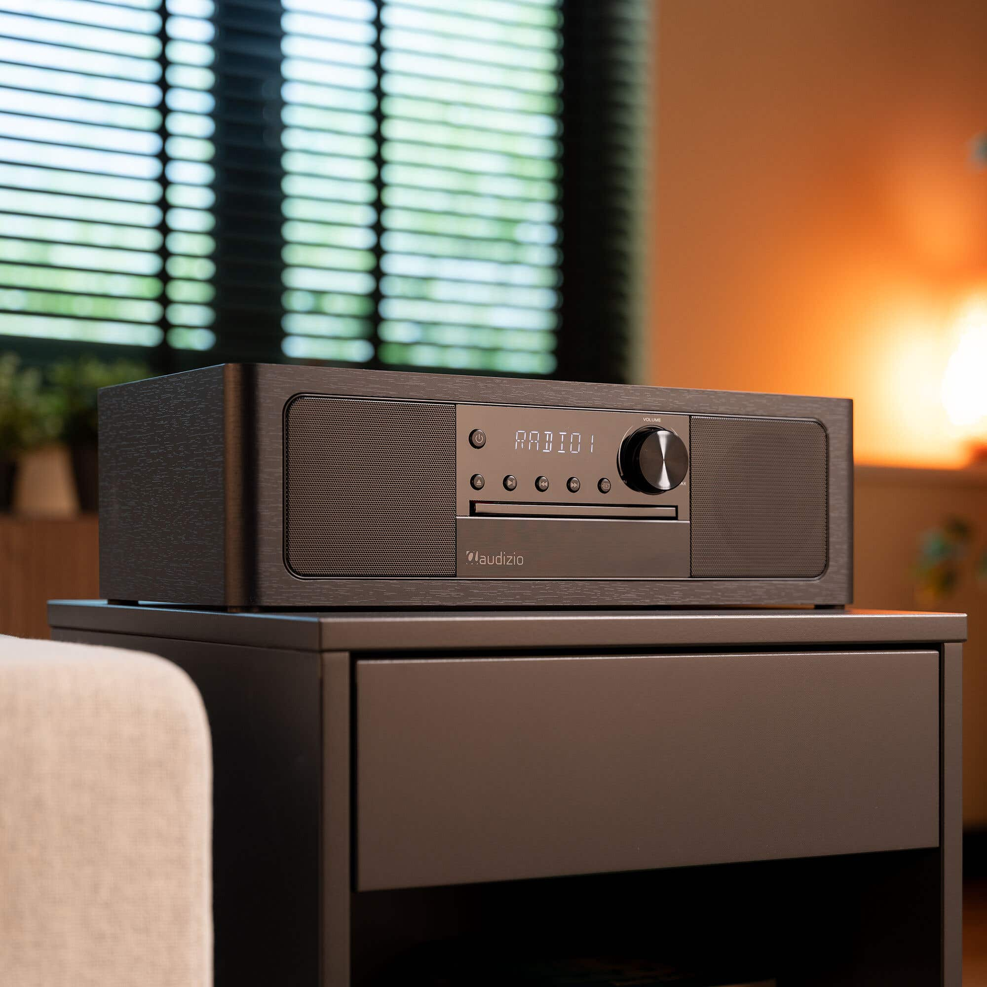 A dark Audizio radio sits on a nightstand, with blinds in the background.