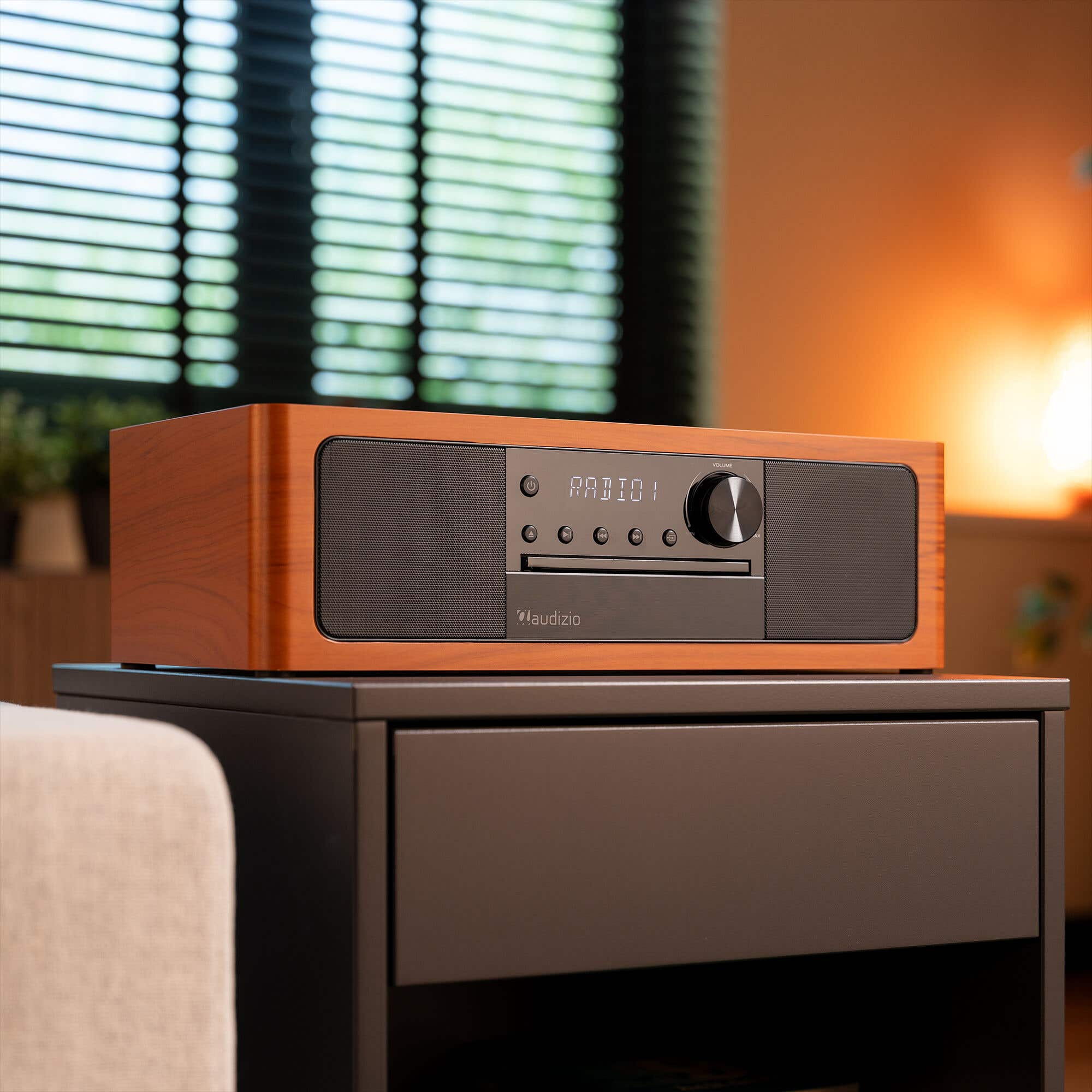 A wooden radio sits on a nightstand with blinds in the background.