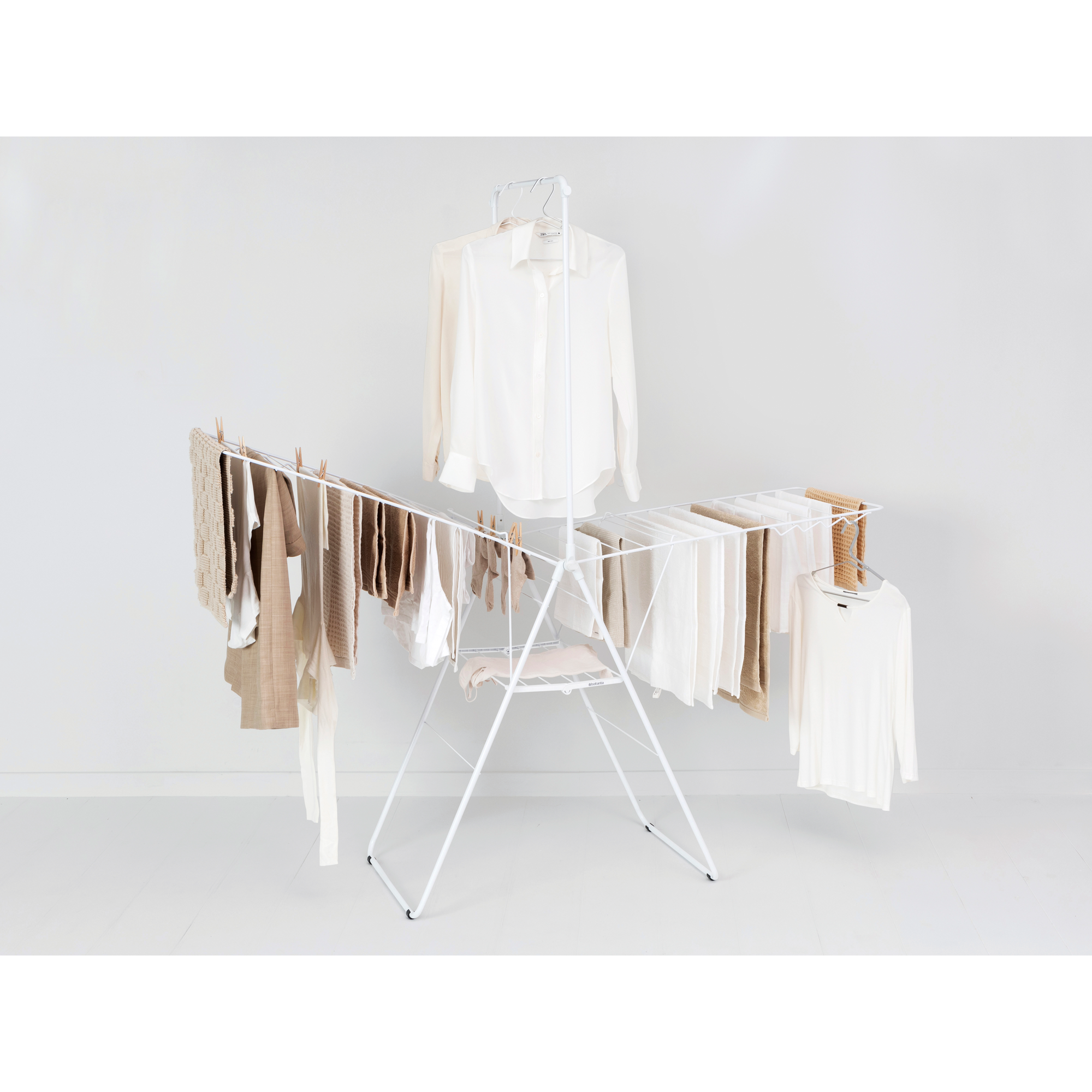 Een wit droogrek met kleding in beige en witte tinten.