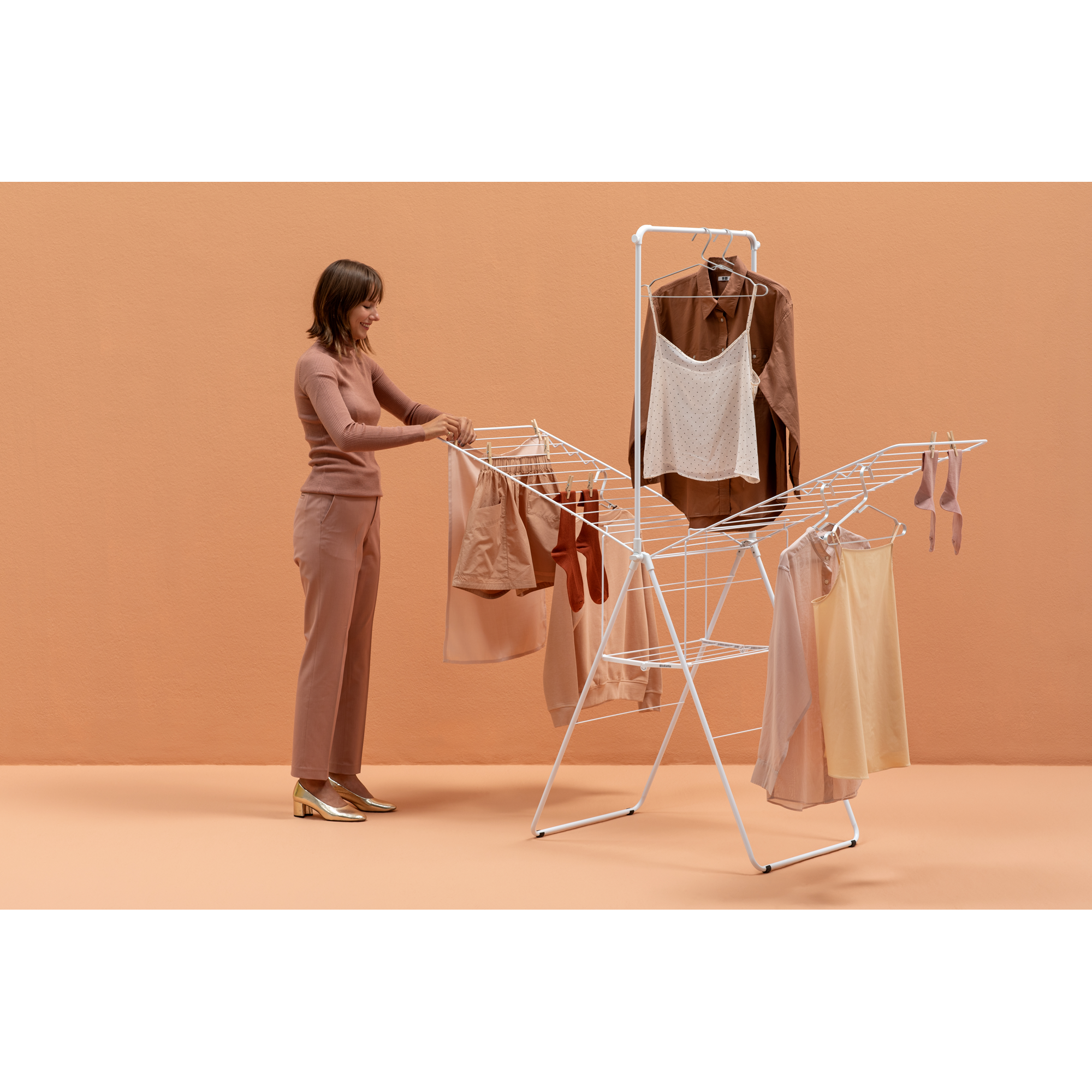 Vrouw hangt kleding op een droogrek. Kleding is beige, bruin en crèmekleurig.