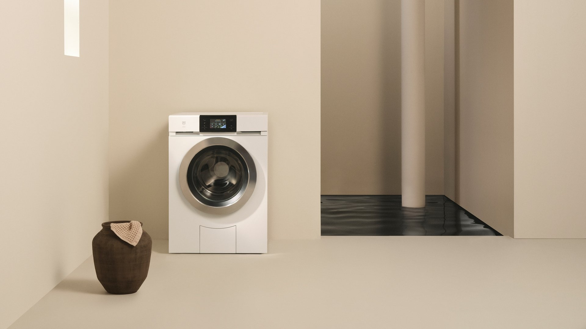 Una lavatrice bianca con una brocca scura accanto su pavimento beige.