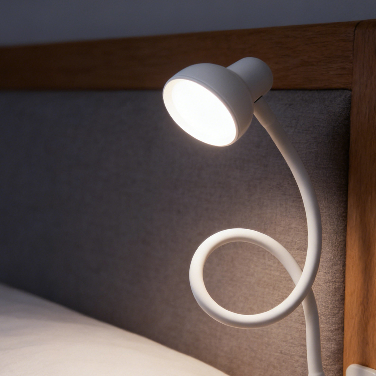 Een witte bedlamp met flexibele arm verlicht een bed.