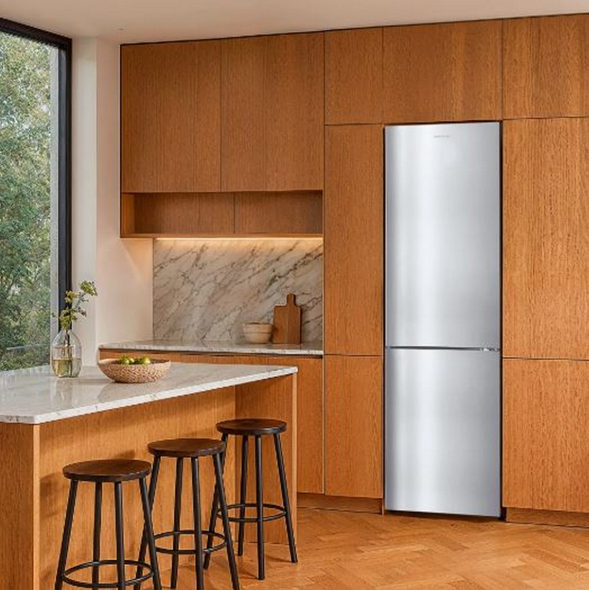 Cocina moderna con gabinetes de madera, refrigerador plateado, salpicadero de mármol.