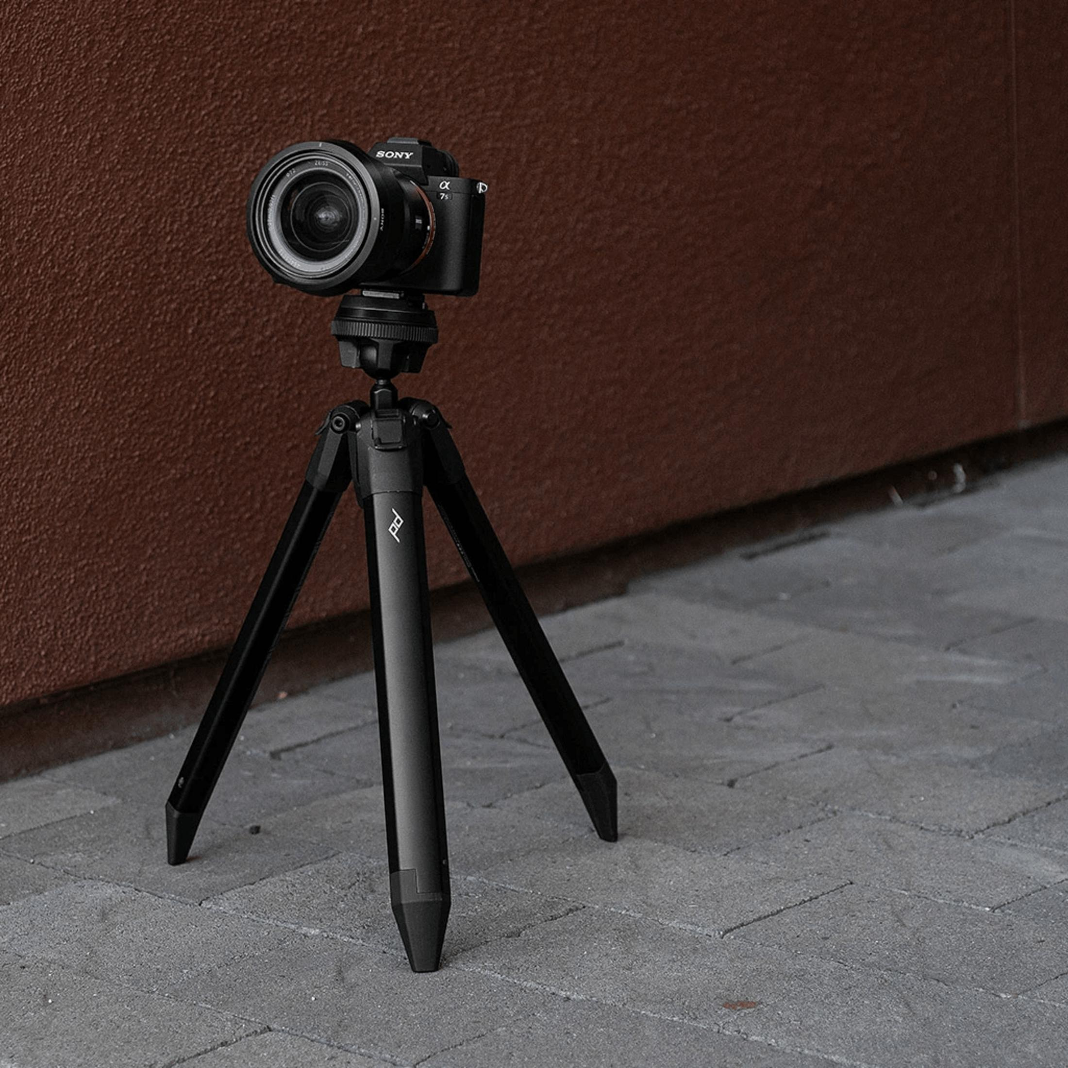 A black Sony camera on a black tripod in front of a brown wall.