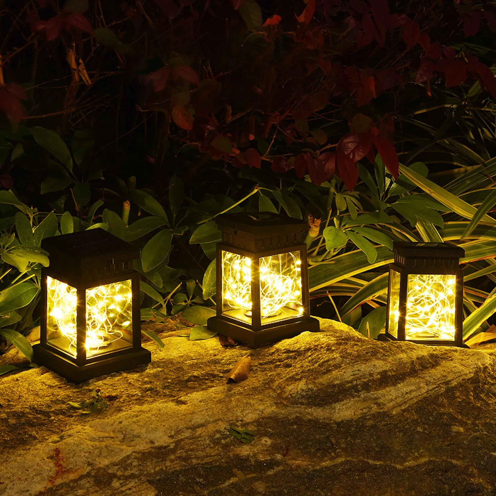 Drei Solar-Laternen mit warmweißen Lichterketten stehen auf einem Felsen.