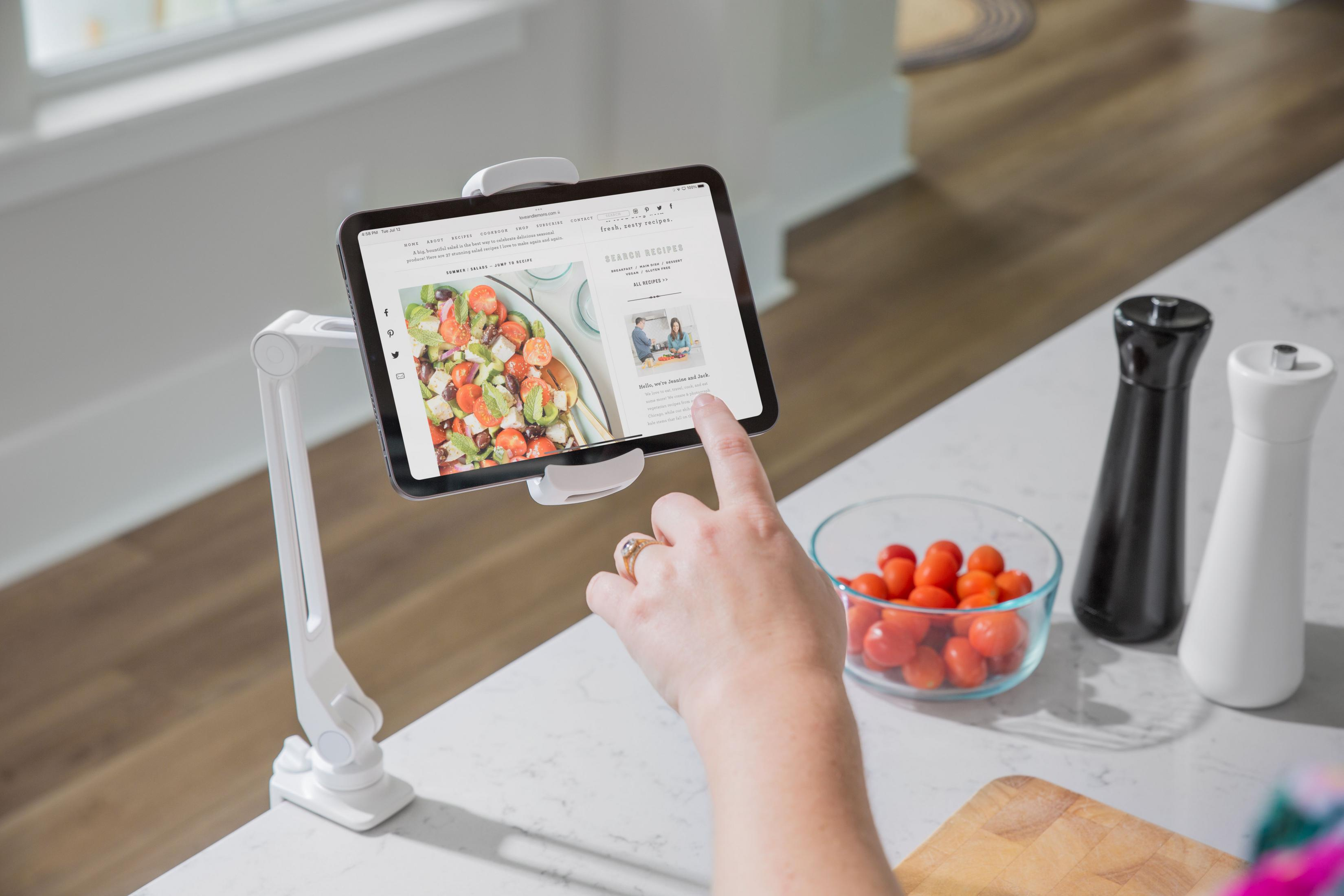 Una mano tocca un tablet che mostra una ricetta. Pomodori e saliere sono vicini.