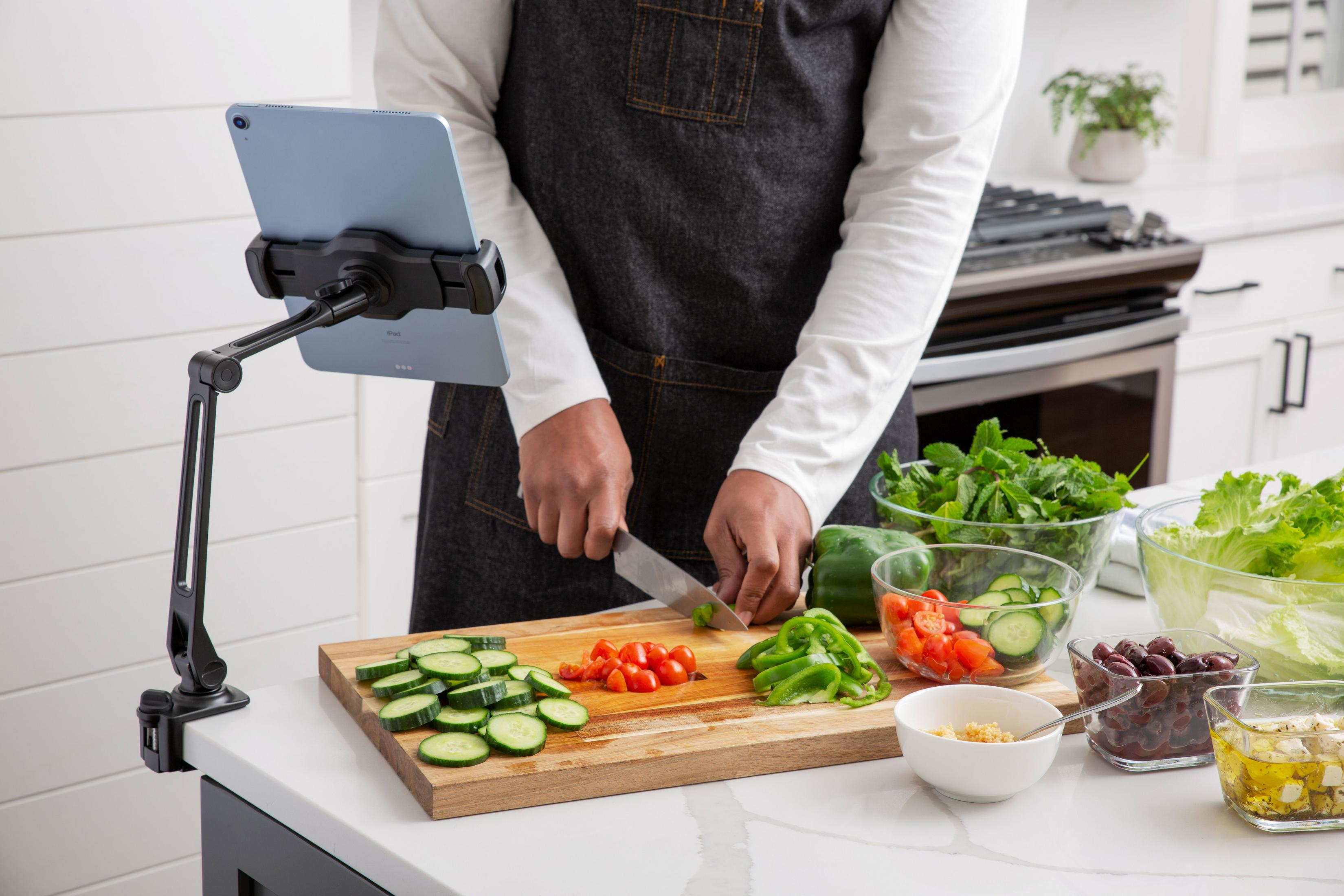 Persona che taglia verdure in cucina con un iPad montato nelle vicinanze.