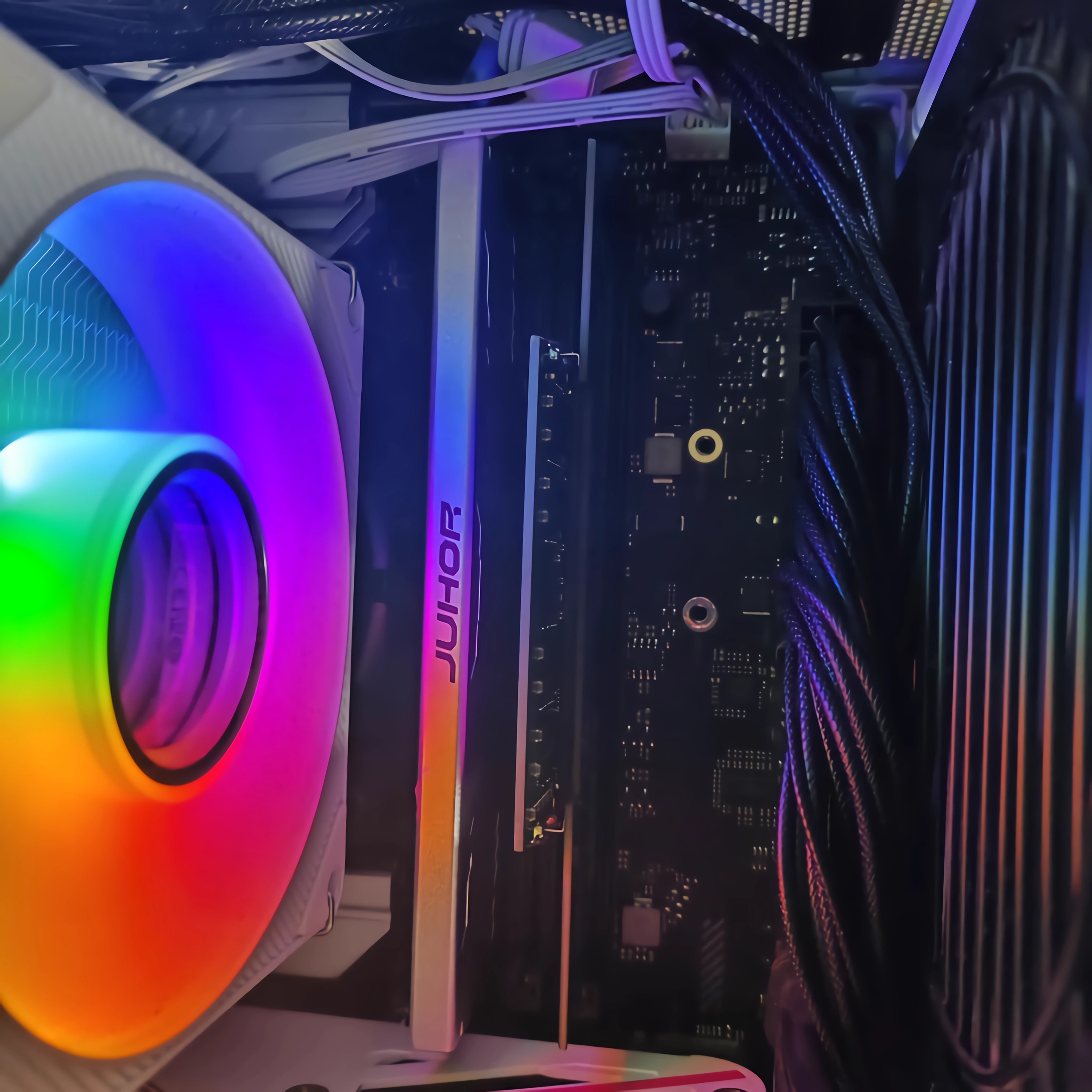 Ein PC-Lüfter mit Regenbogen-LEDs neben einer RAM-Karte und Kabeln.