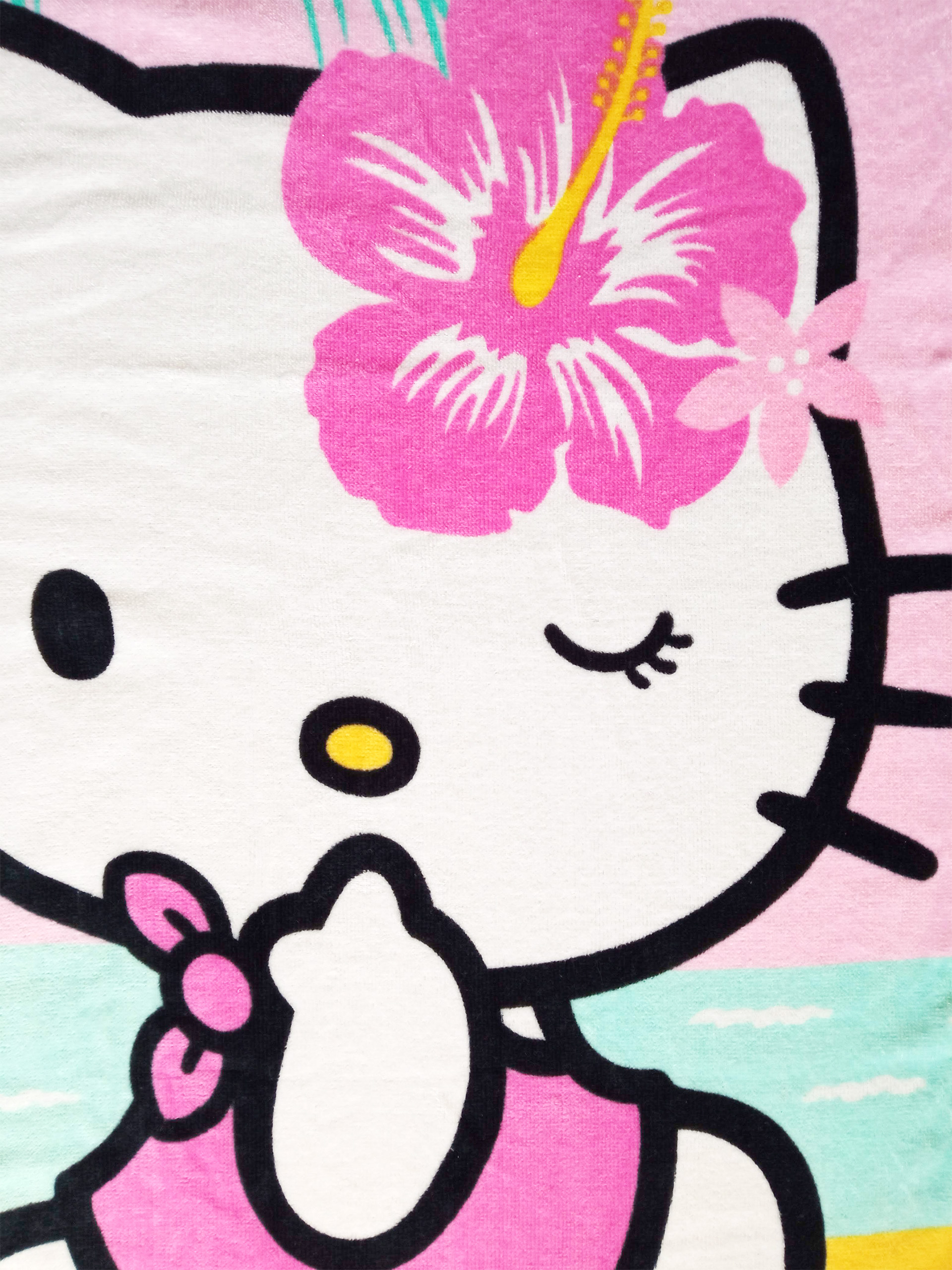 Hello Kitty mit einer Hibiskusblume im Haar, einem rosa Kleid und einem Meer im Hintergrund.