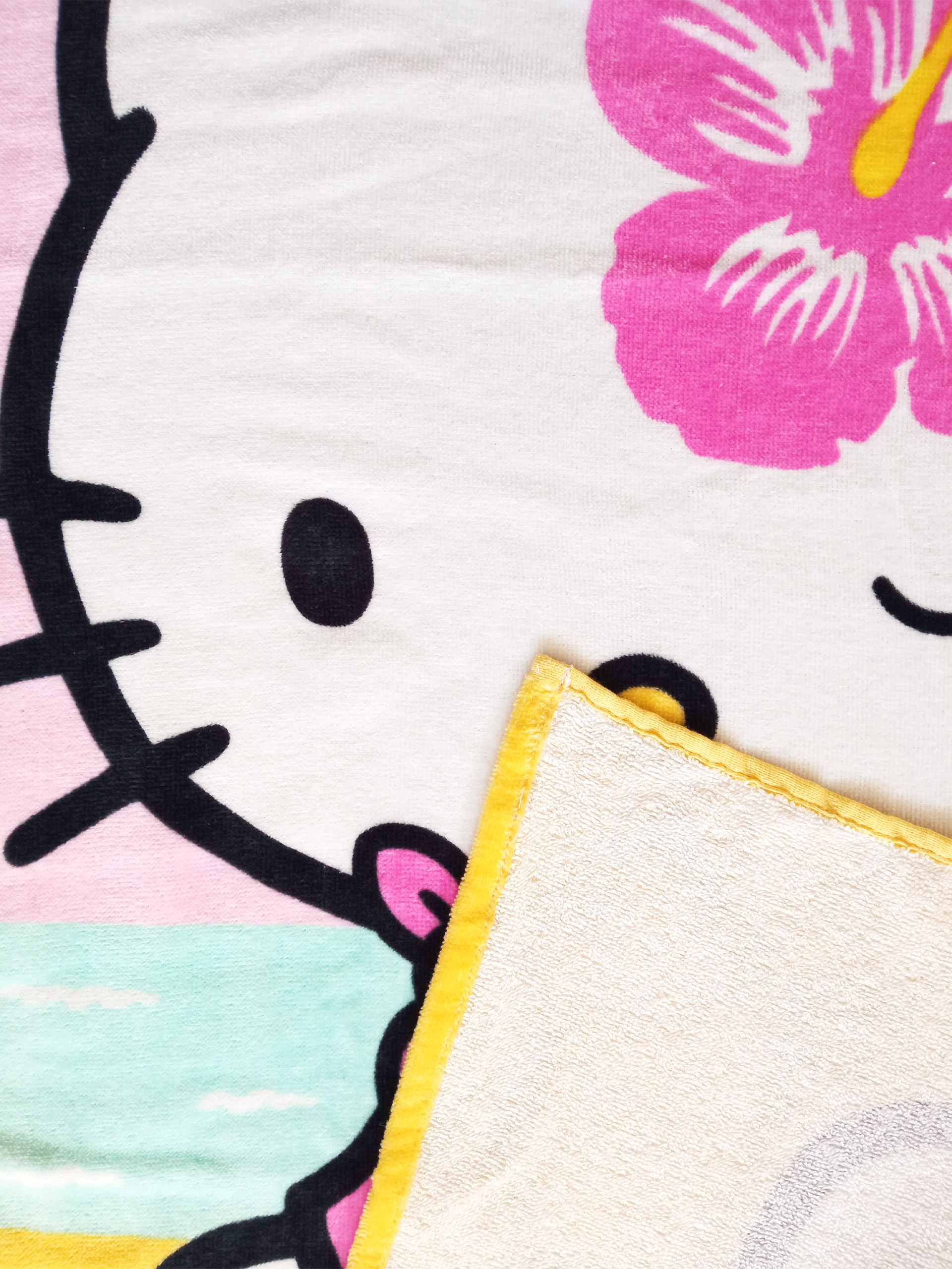Hello Kitty mit rosa Blume auf weißem Handtuch mit gelbem Rand.