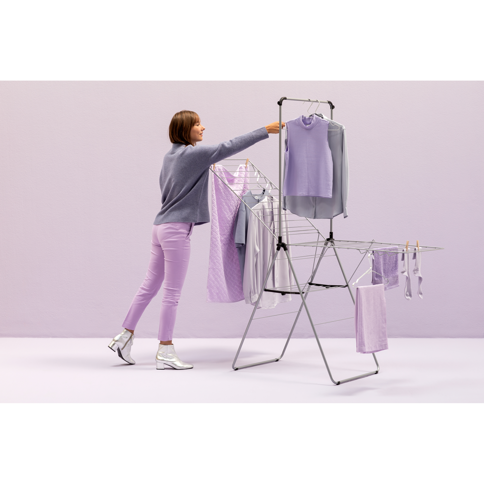 A woman hangs purple clothes on a drying rack against a lavender wall.