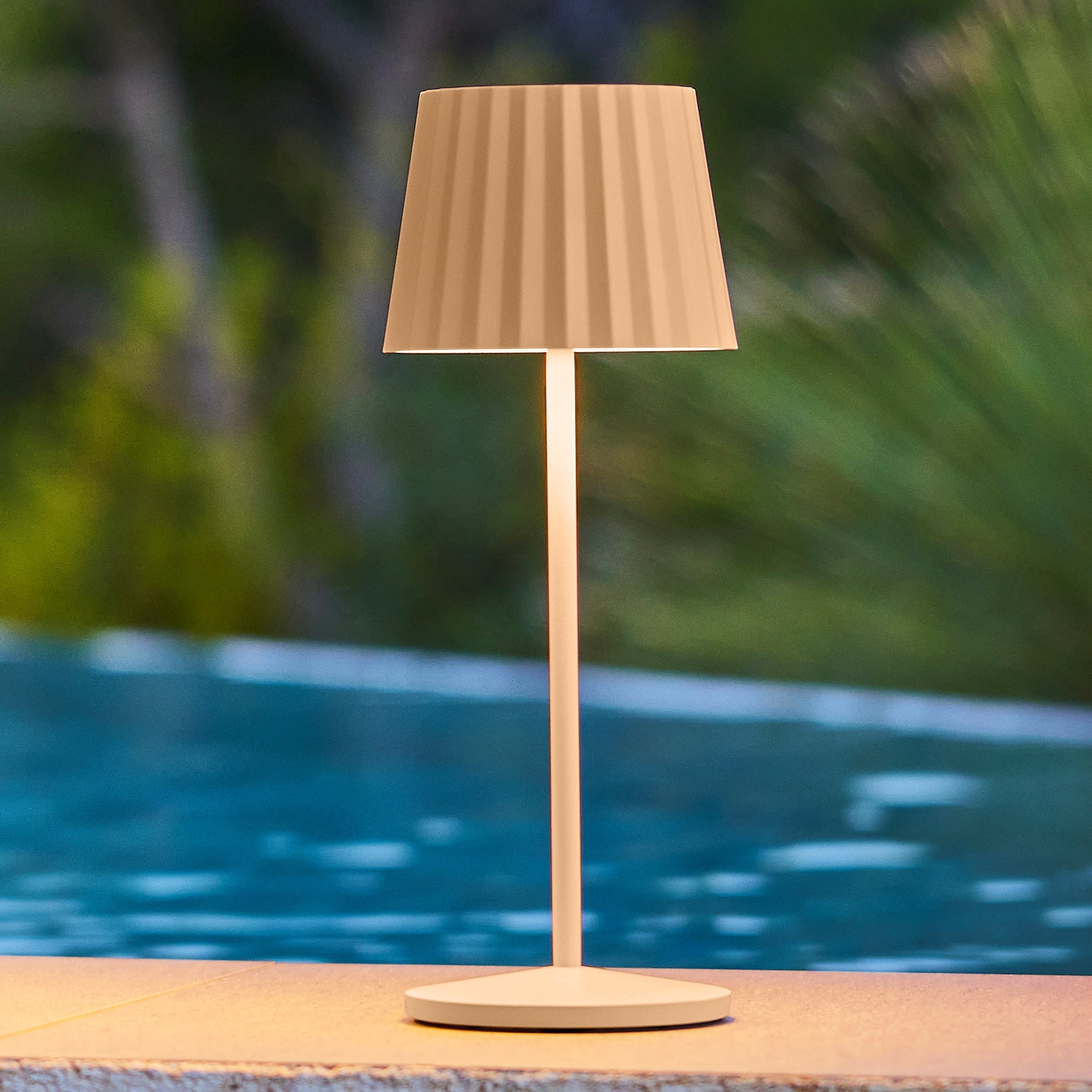 Eine Tischlampe mit geripptem Schirm steht am Pool.
