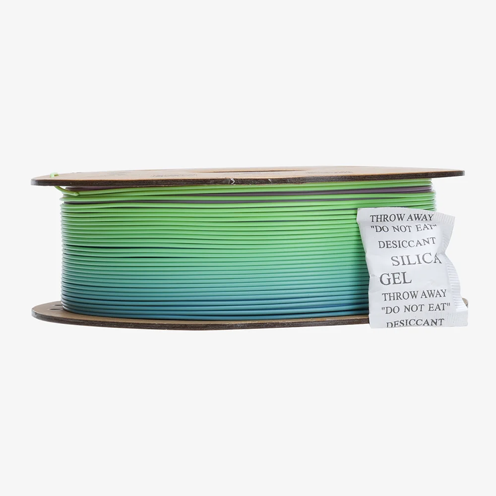 Un rocchetto di filamento per stampante 3D in gradiente dal verde al blu, con bustina di gel di silice.