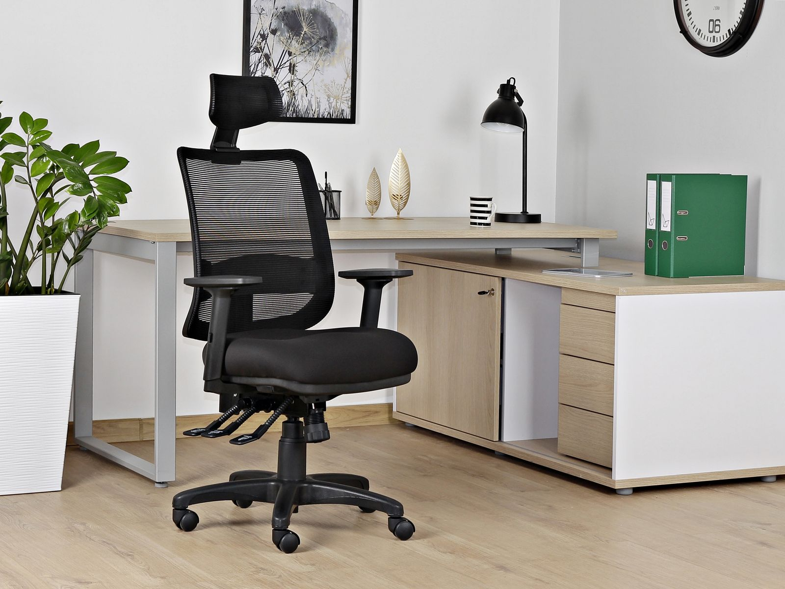 Czarny fotel biurowy stoi przed biurkiem z roślinami i segregatorami.