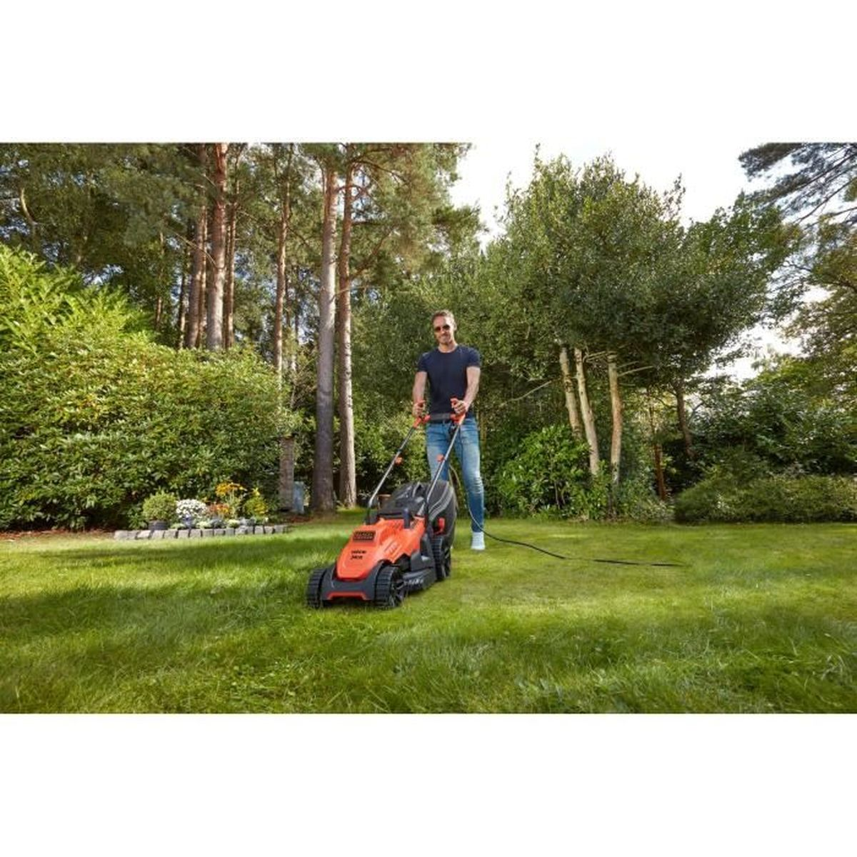 Mann mäht Rasen mit einem orangefarbenen Rasenmäher in einem üppigen Garten.
