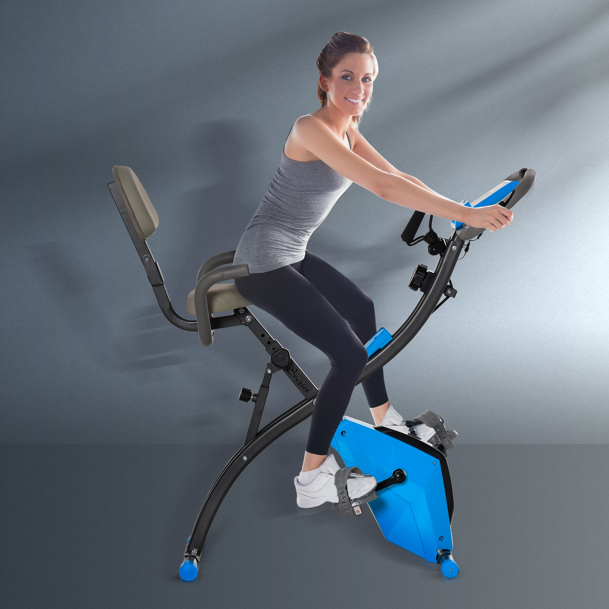Frau trainiert auf einem blauen Heimtrainer vor grauem Hintergrund.