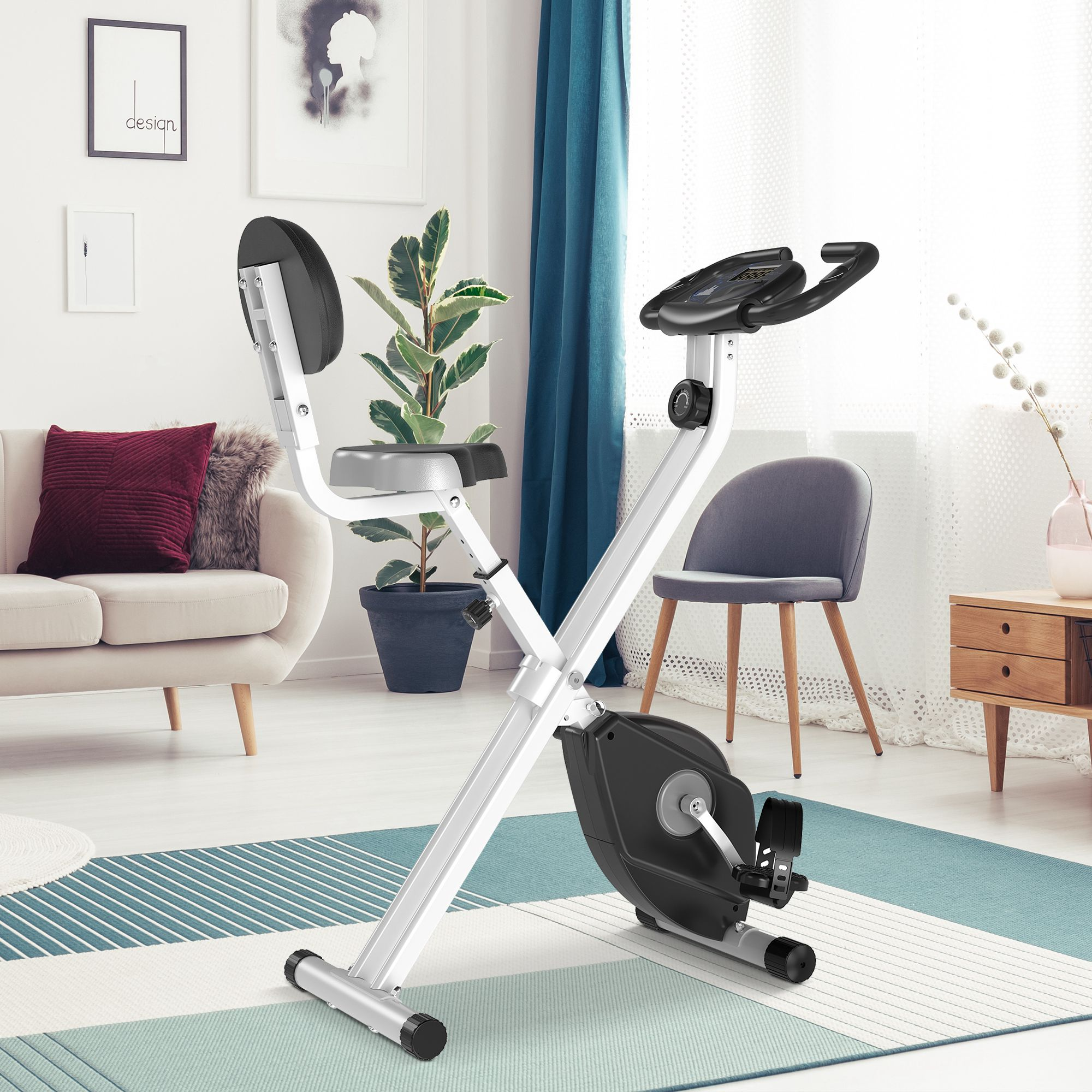 Ein weißes, zusammenklappbares Heimtrainer in einem Wohnzimmer mit Sofa und Pflanzen.