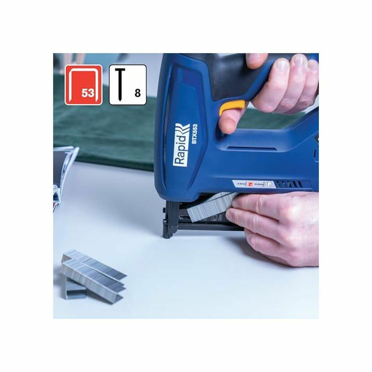 Blaue Rapid-Klammerpistole mit gelbem Auslöser, Klammern und zwei Händen.