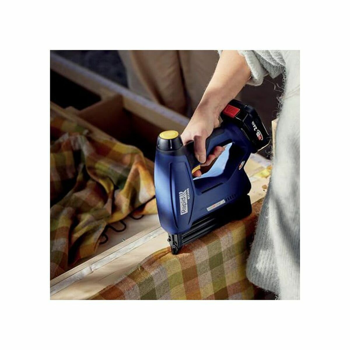Eine blaue Nagelpistole wird verwendet, um Stoff an Holz zu befestigen.