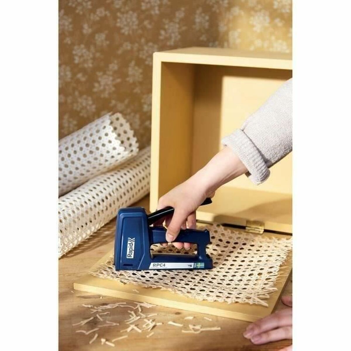 Una mano usa una sparapunti blu per fissare un materiale a rete a una scatola di legno.
